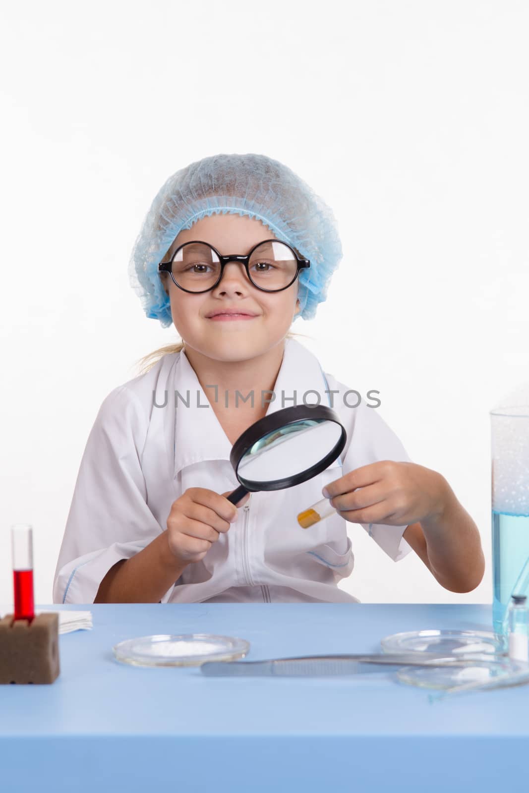 Chemist girl sitting at the table with the reagents in chemistry class and puts experiments