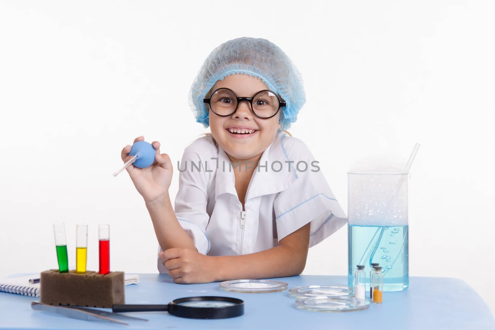 Chemist girl sitting at the table with the reagents in chemistry class and puts experiments