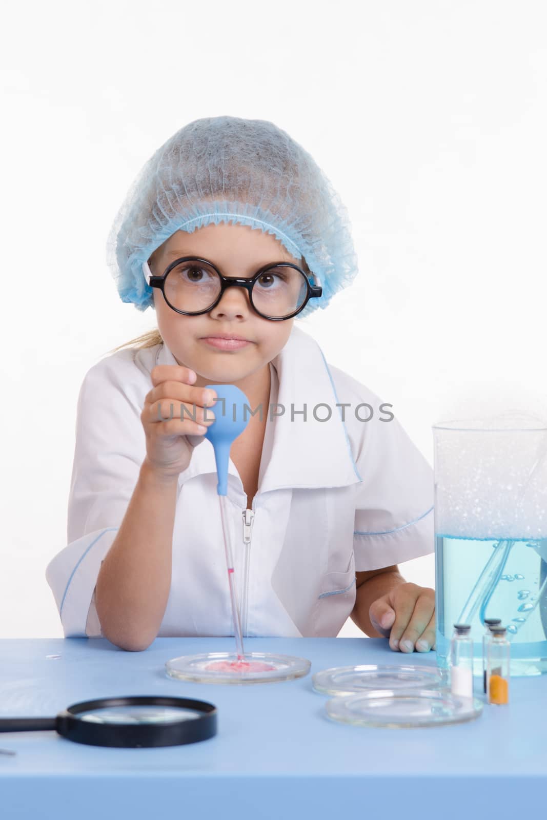 Chemist girl sitting at the table with the reagents in chemistry class and puts experiments