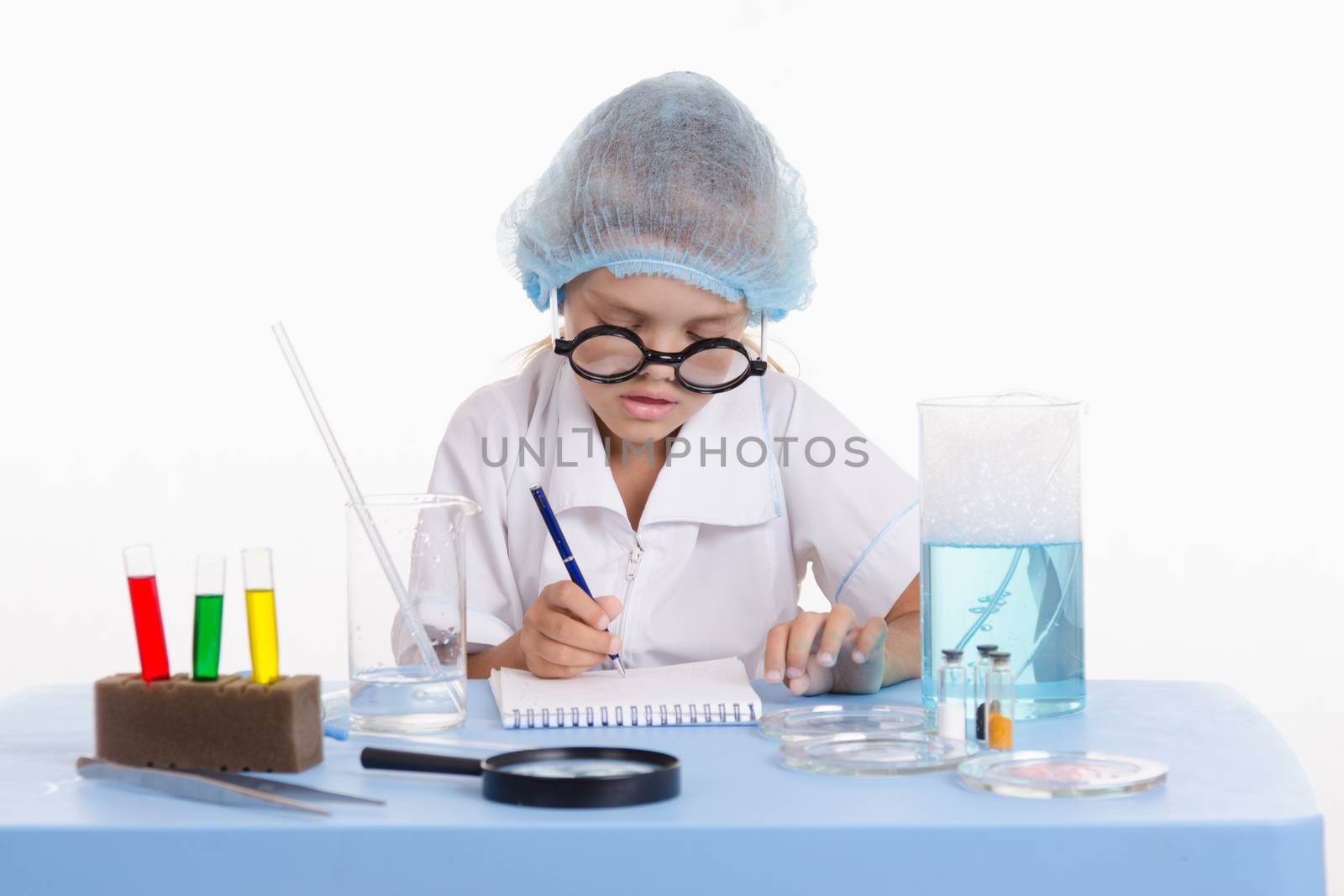 Chemist girl sitting at the table with the reagents in chemistry class and puts experiments