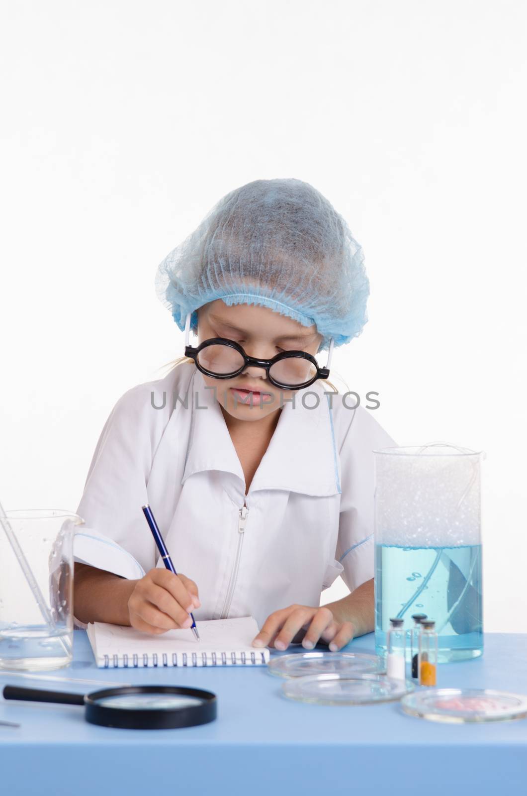 Chemist girl sitting at the table with the reagents in chemistry class and puts experiments