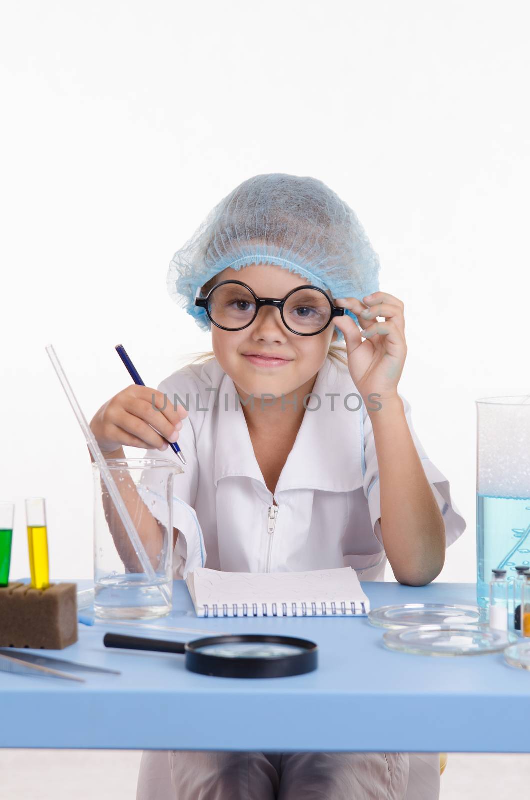 Chemist girl sitting at the table with the reagents in chemistry class and puts experiments