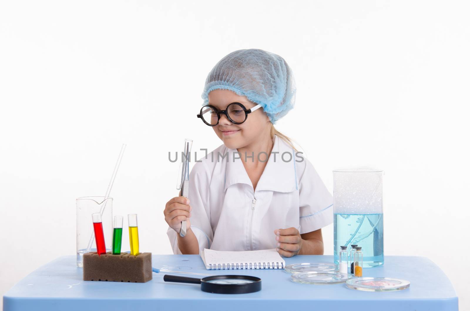 Chemist girl sitting at the table with the reagents in chemistry class and puts experiments