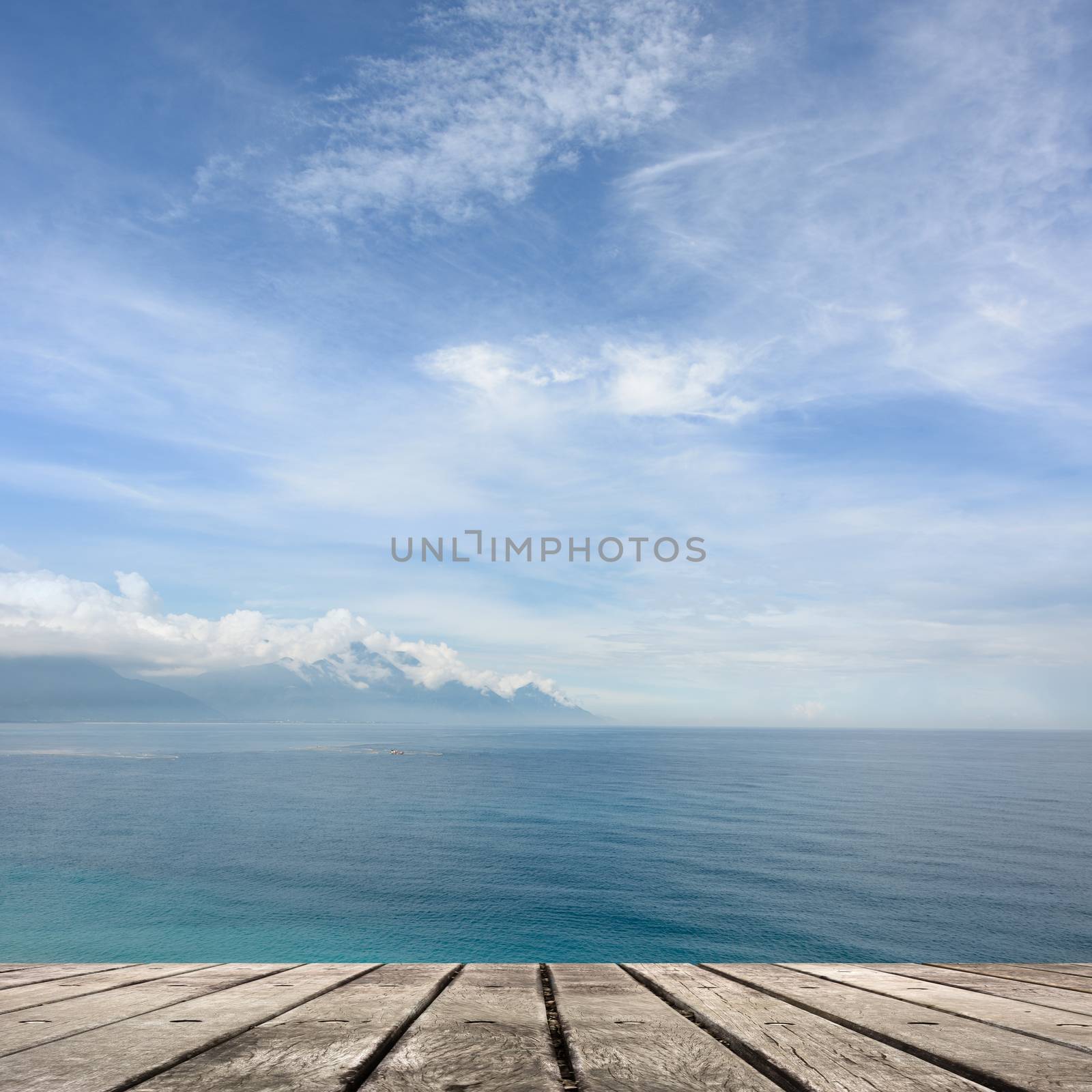 Empty wooden deck table with copyspace under sunny cloudy sky in the beach, focus on the wooden ground.