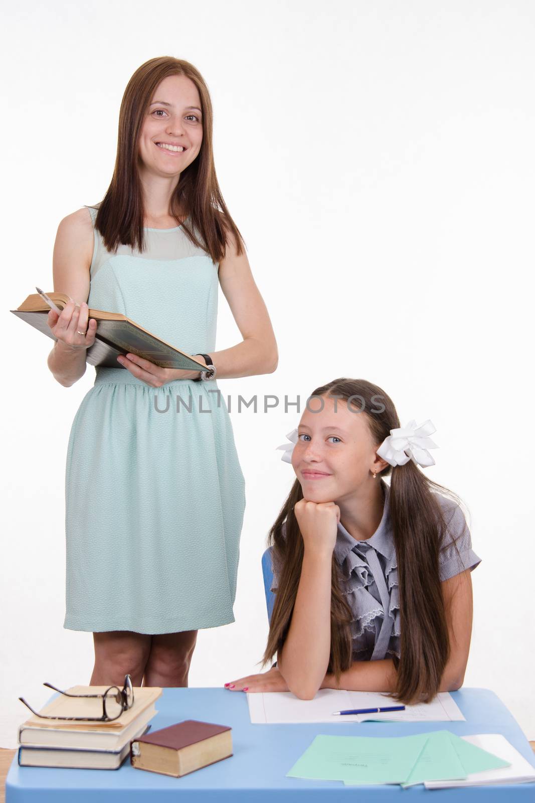 Teacher standing at desk behind which sits a diligent student