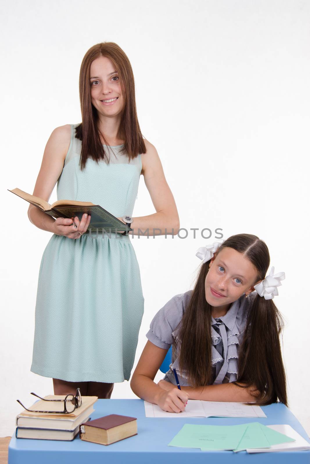Teacher standing at desk behind which sits a diligent student