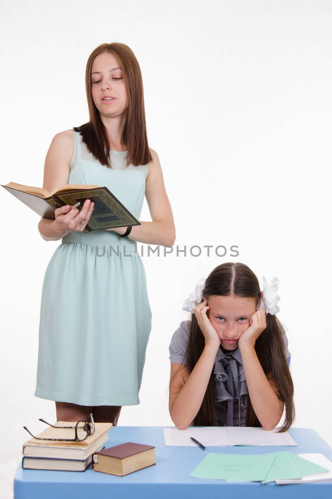Teacher standing at desk behind which sits a tired student