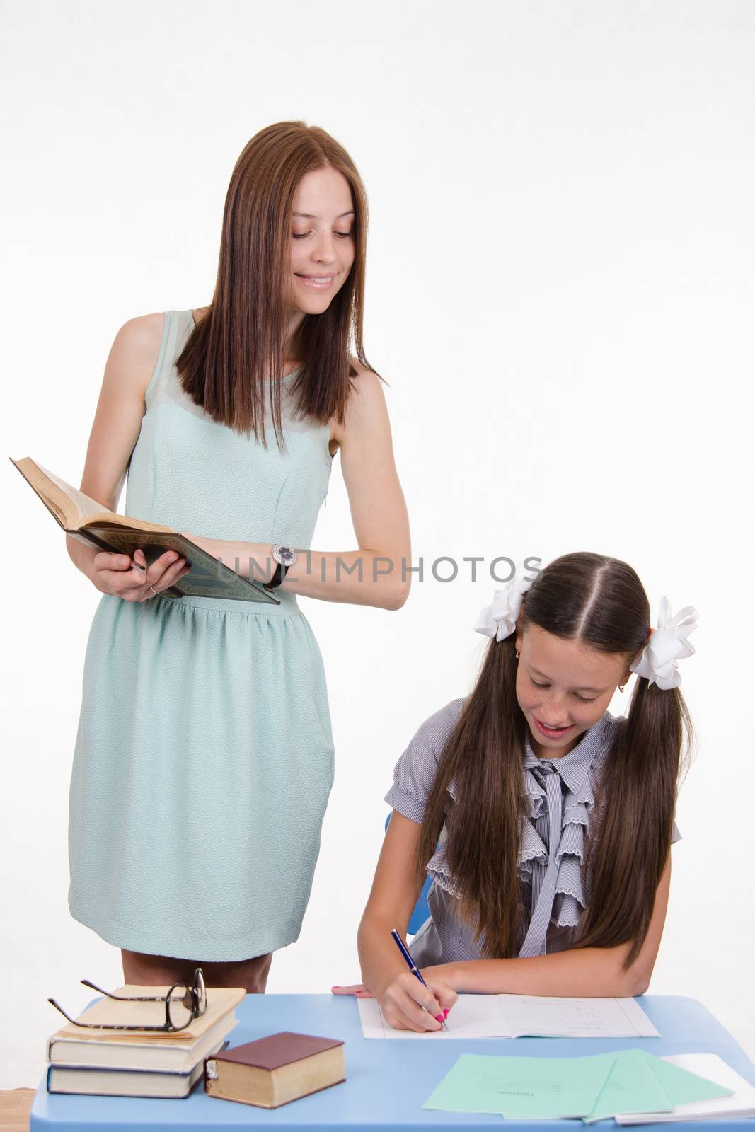 Teacher standing at desk behind which sits a diligent student