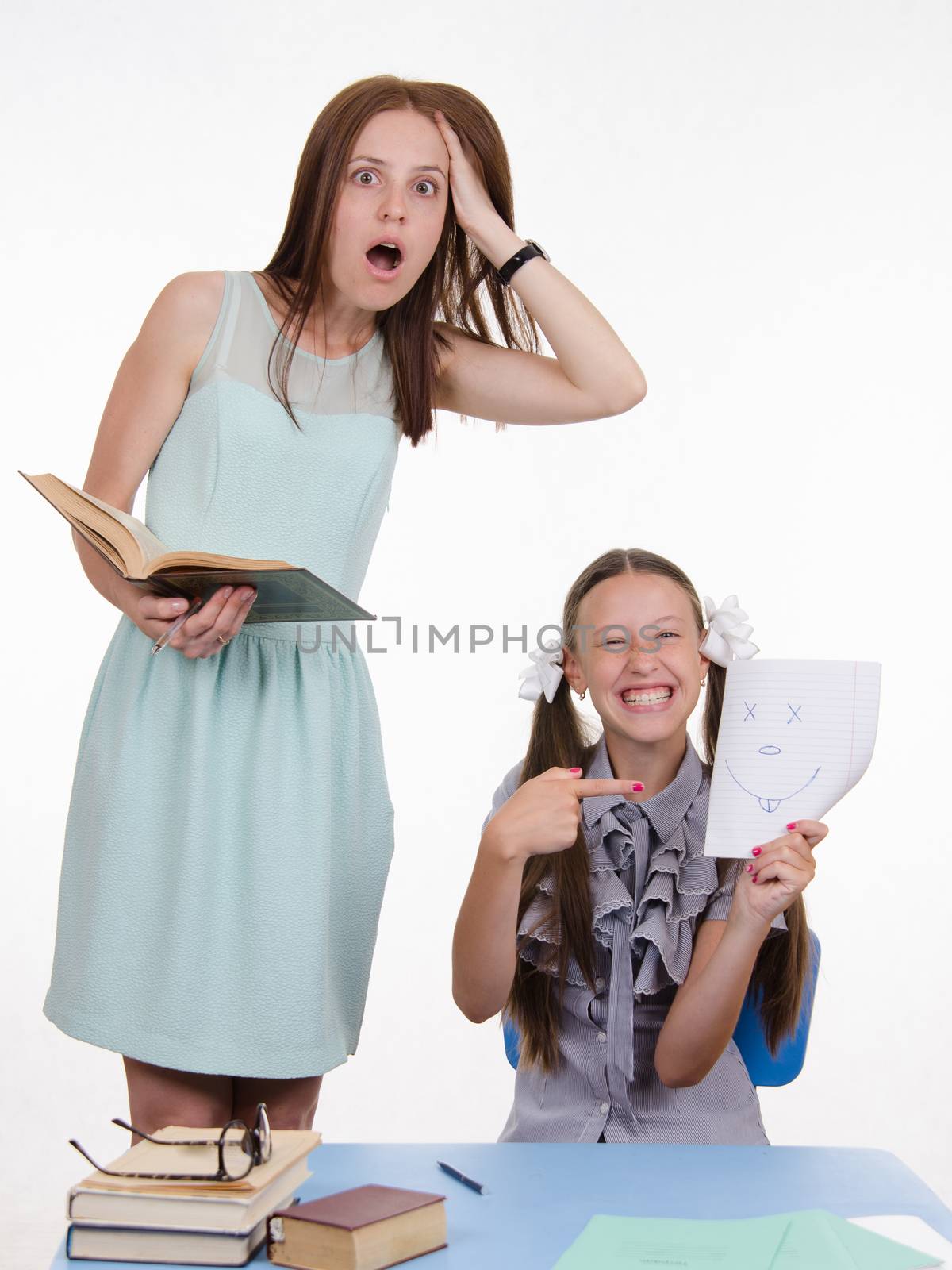 Teacher standing at desk behind which sits student who drew a funny face in a notebook