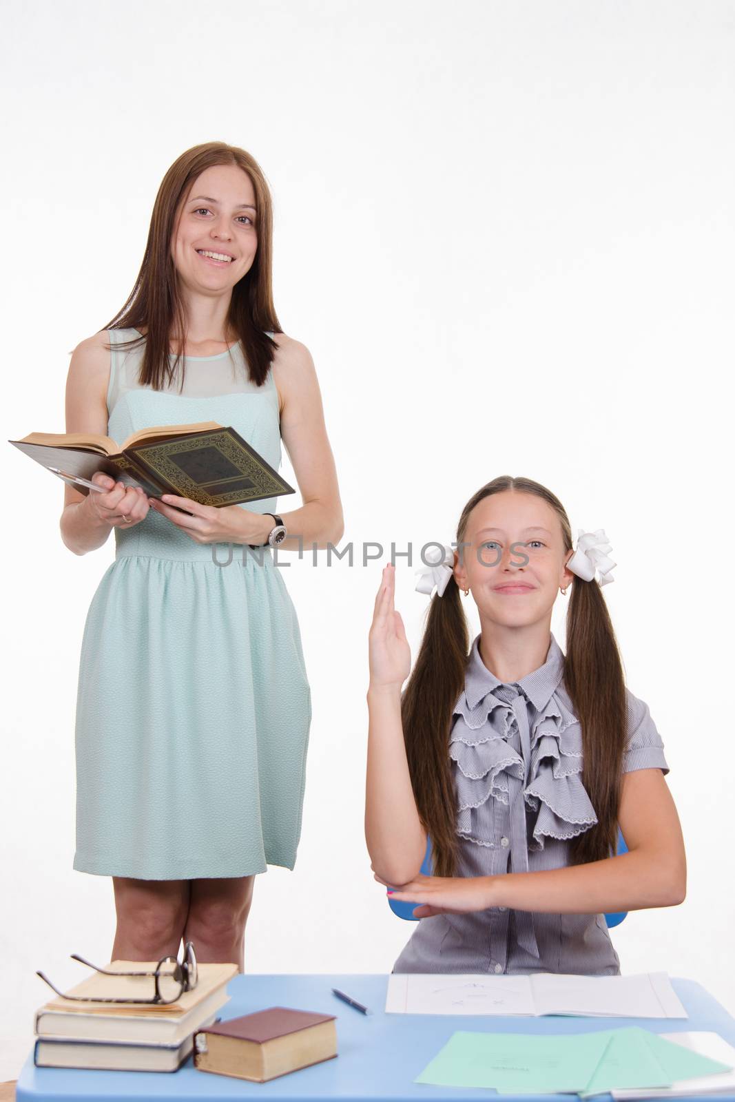 Teacher standing at desk behind which sits a diligent student