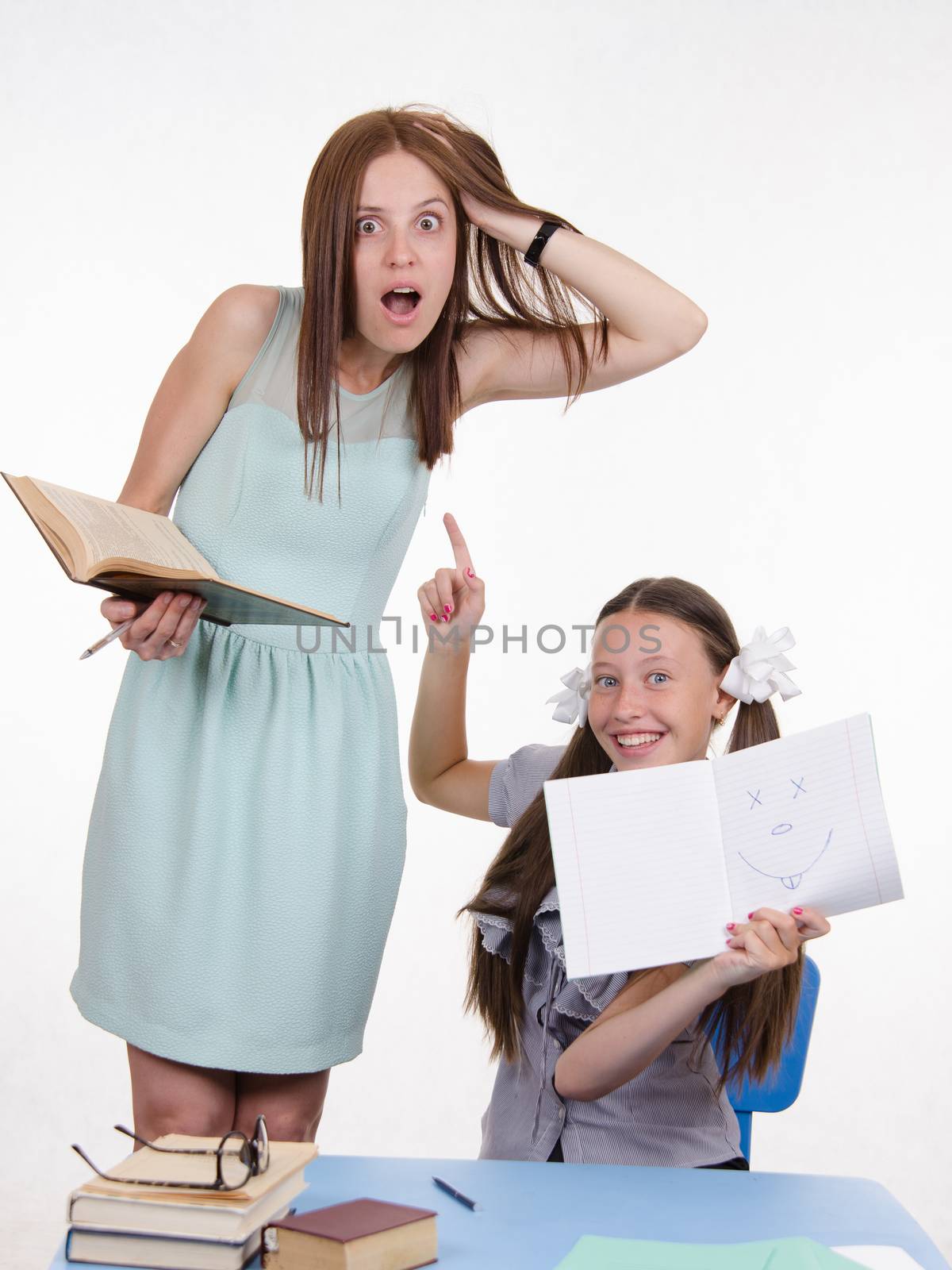 Teacher standing at desk behind which sits student who drew a funny face in a notebook