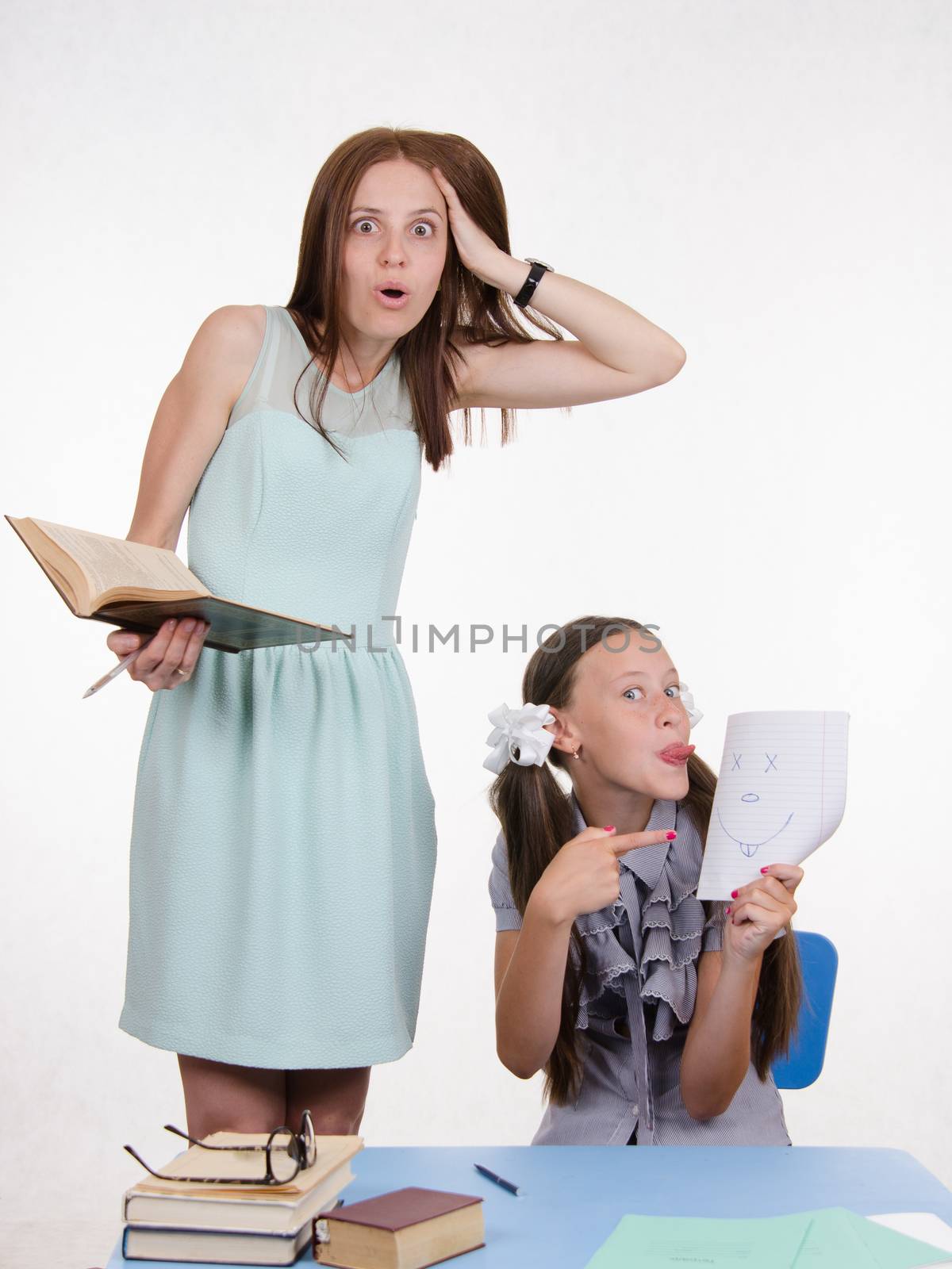 Teacher standing at desk behind which sits student who drew a funny face in a notebook