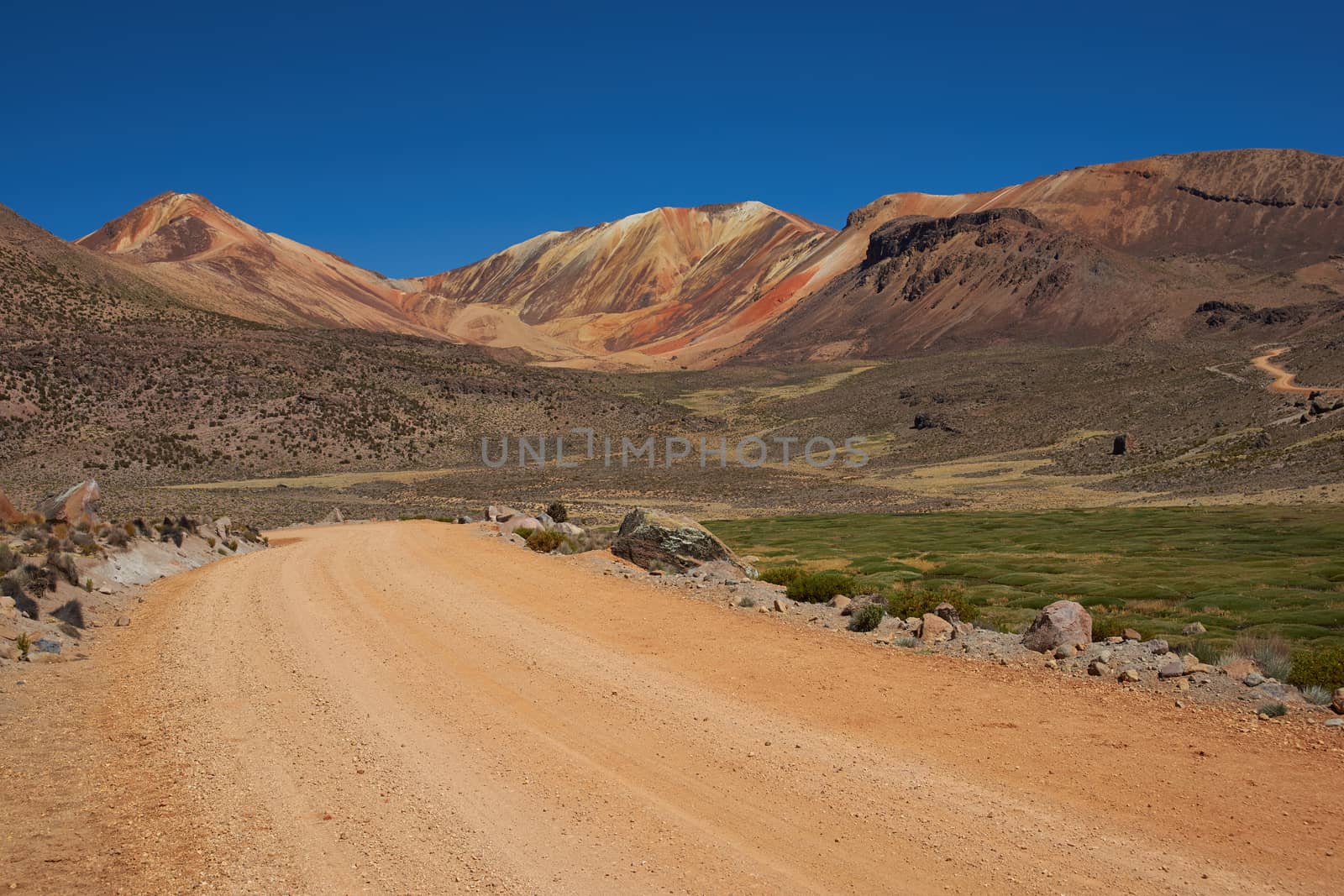 Orange coloured gravel road running through naturally coloured mountains high in the Atacama Desert of north east Chile. The altitude is in excess of 4,000 metres.
