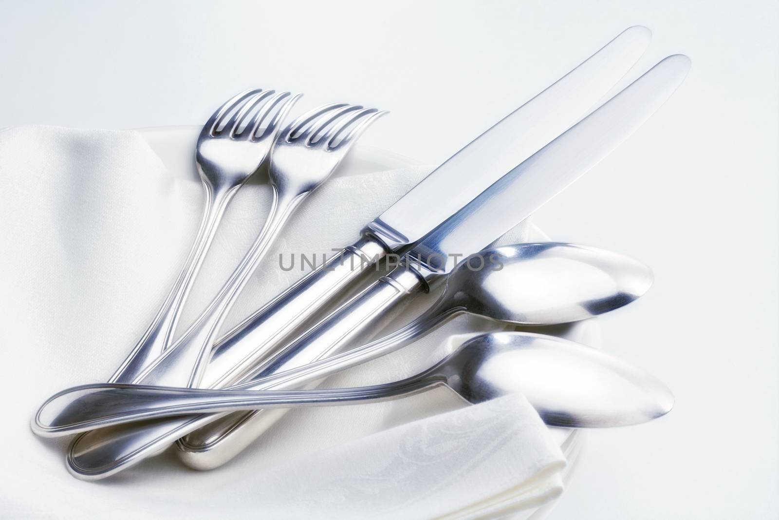 closeup of silverware on pile of plates with white cloth