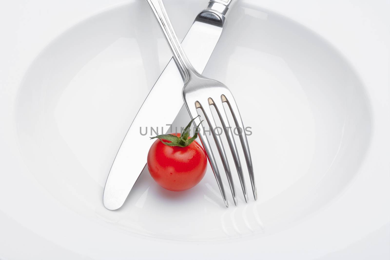 cherry tomato on a plate with fork and knife isolated on white