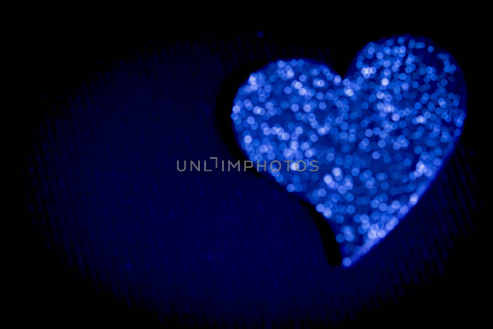 Defocused blue heart on black background.