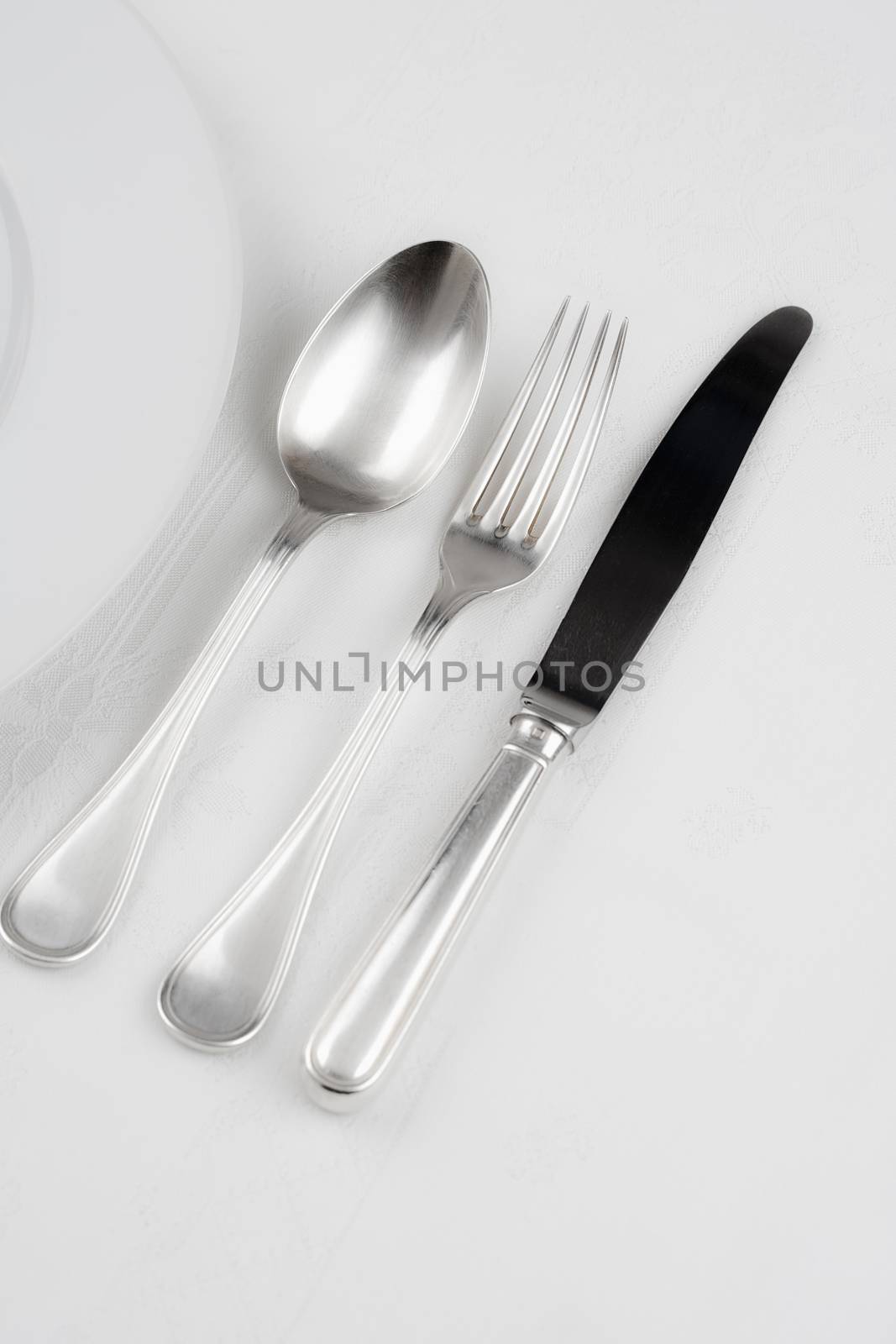silverware - knife, fork and spoon next to a plate on white cloth
