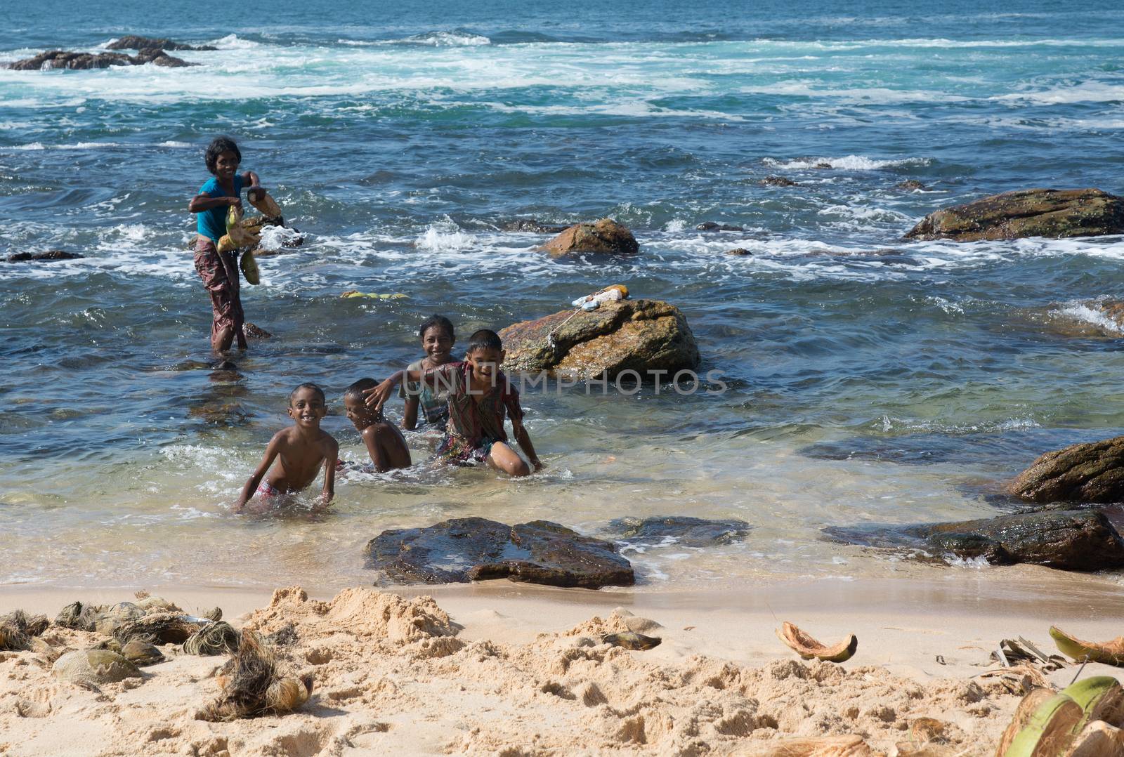 TANGALLE, SOUTHERN PROVINCE, SRI LANKA - DECEMBER 16, 2014: Sinhalese woman, boys and girl washing coconuts in the warm water on paradise beach on December 16 2014, in Tangalle, Sri Lanka.