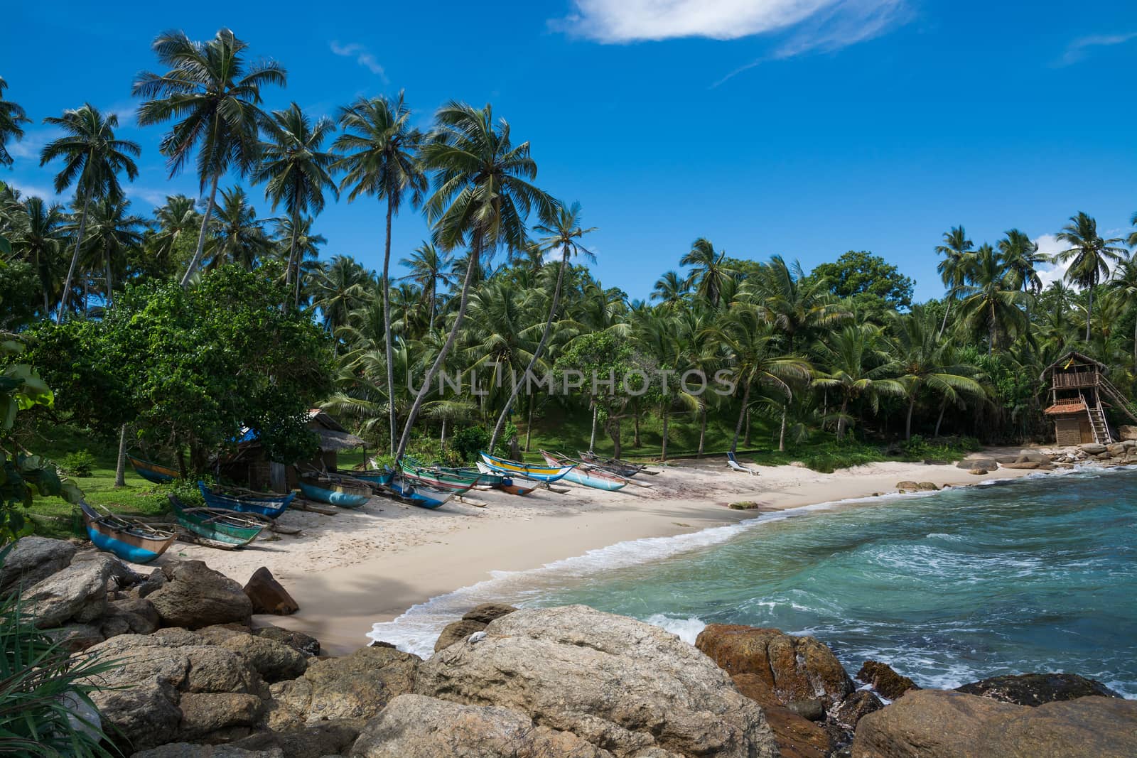 Tropical rocky beach with coconut palm trees, sandy beach and traditional fishing boats. Rocky Point, Tangalle, Southern Province, Sri Lanka, Asia.