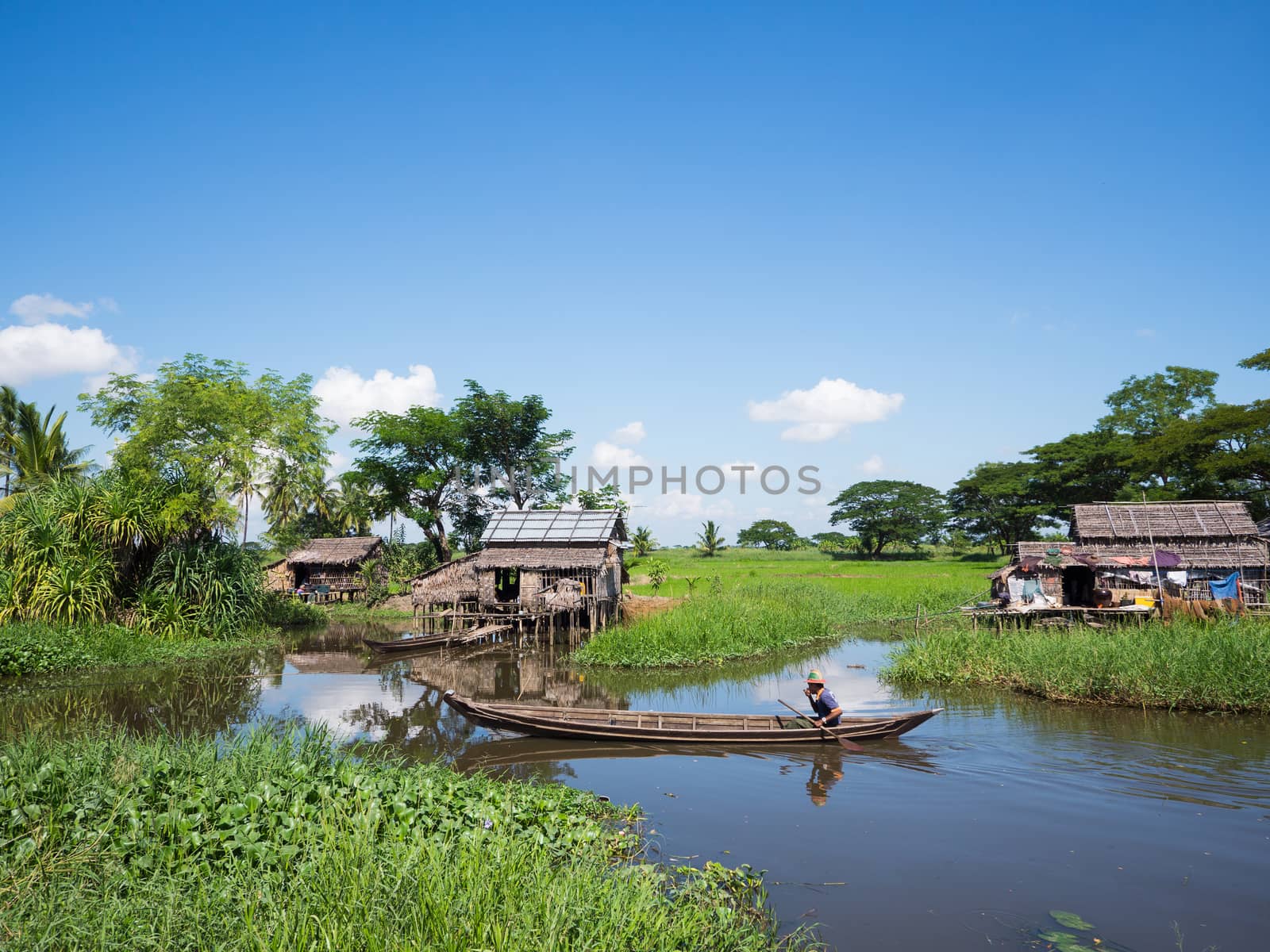 MAUBIN, MYANMAR - NOVEMBER 12, 2014: Man paddling past farmers' houses in Maubin, Ayeyarwady Division in Southwest Myanmar. Many homes in the area lack road connection and can only be reached by boat.