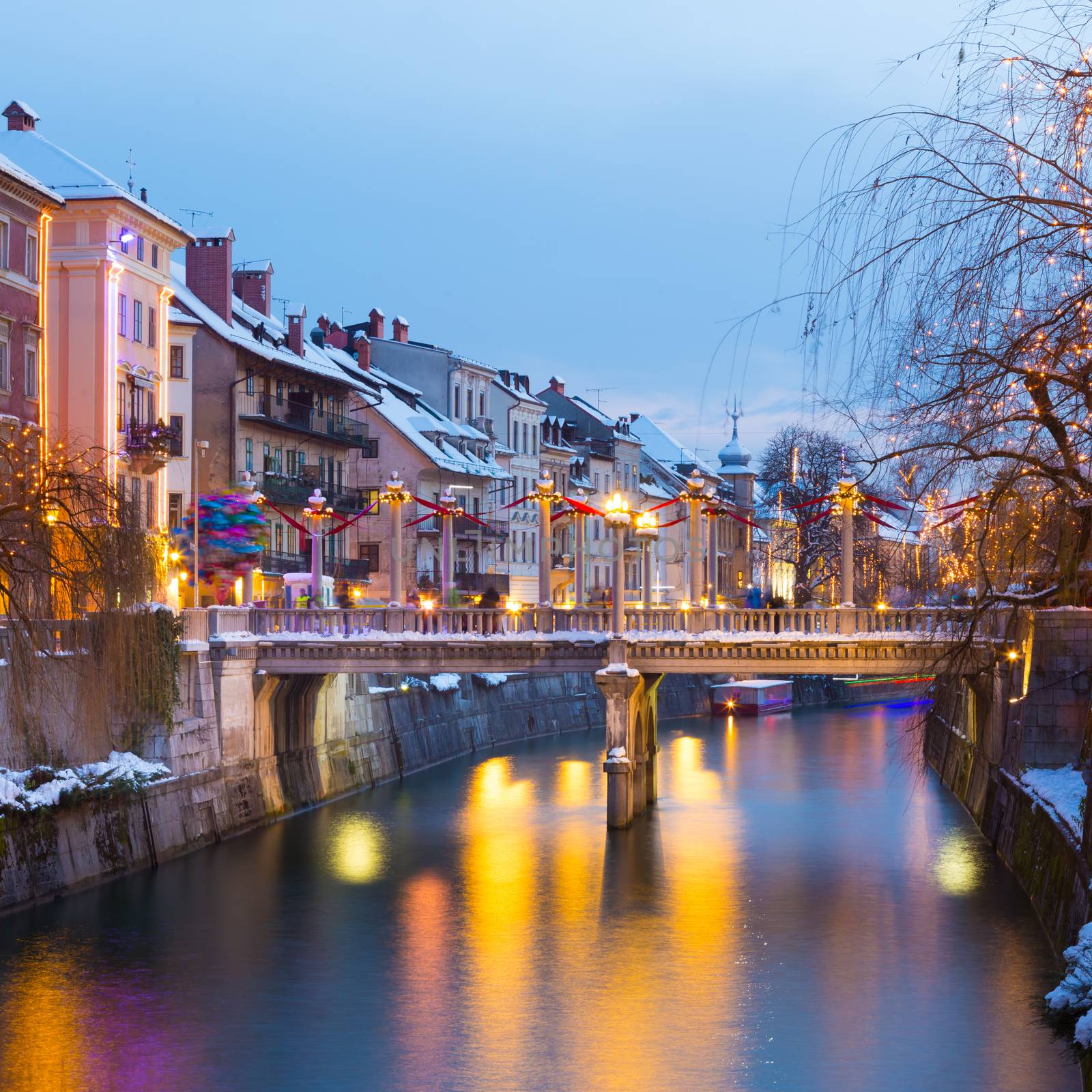View of lively river Ljubljanica bank with Cobblers' Bridge in old city center decorated with Christmas lights. Ljubljana, Slovenia, Europe. Shot at dusk.