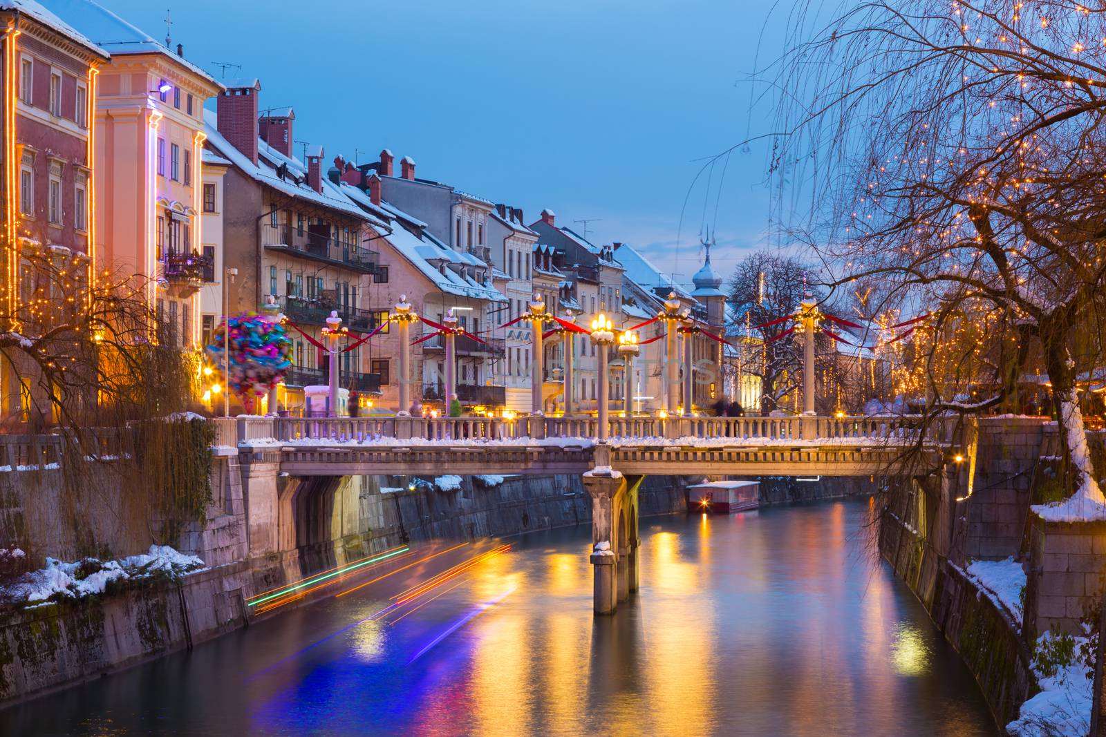 View of lively river Ljubljanica bank with Cobblers' Bridge in old city center decorated with Christmas lights. Ljubljana, Slovenia, Europe. Shot at dusk.
