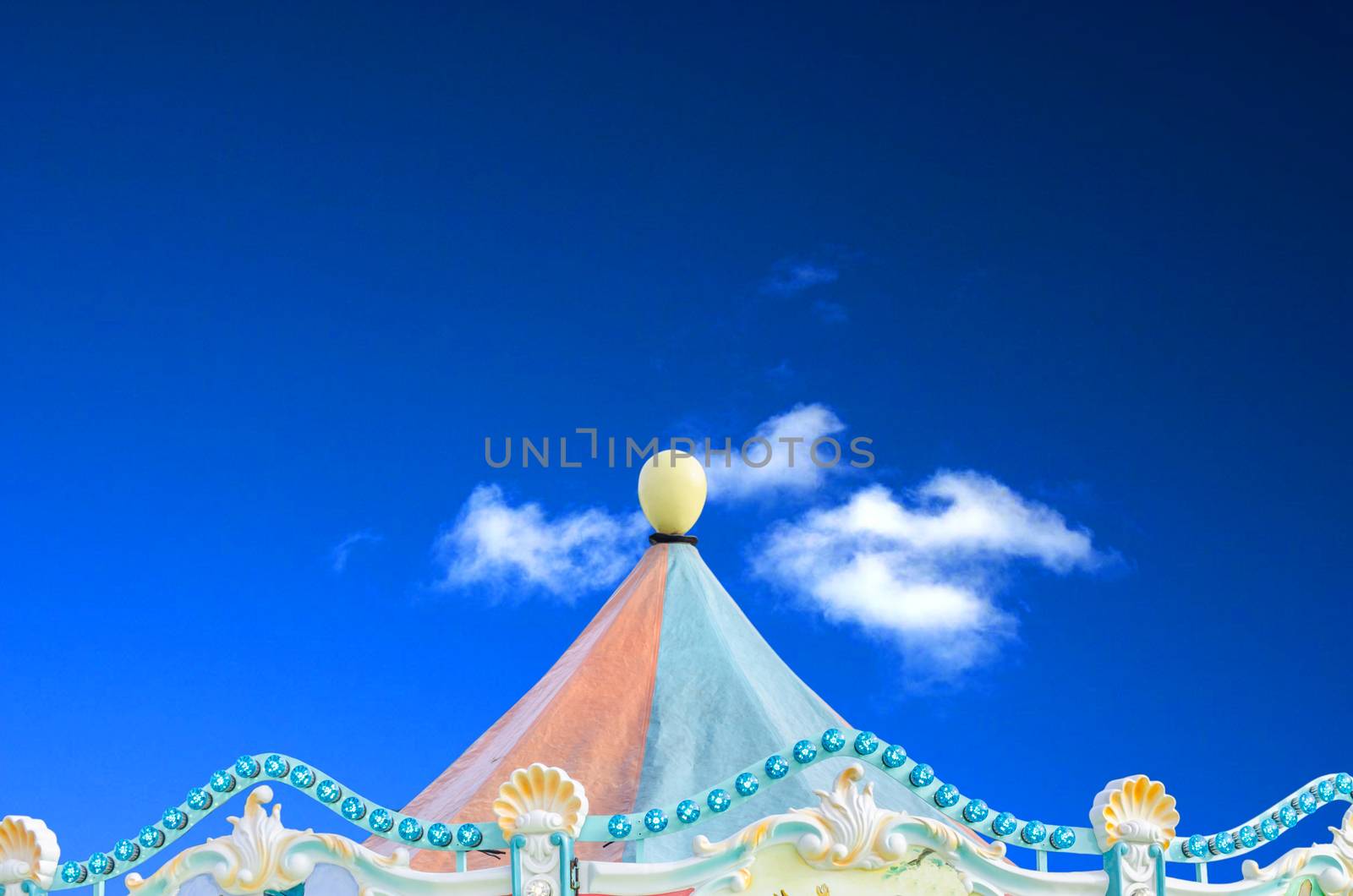 Circus carnival tent in front of a blue sky with clouds.