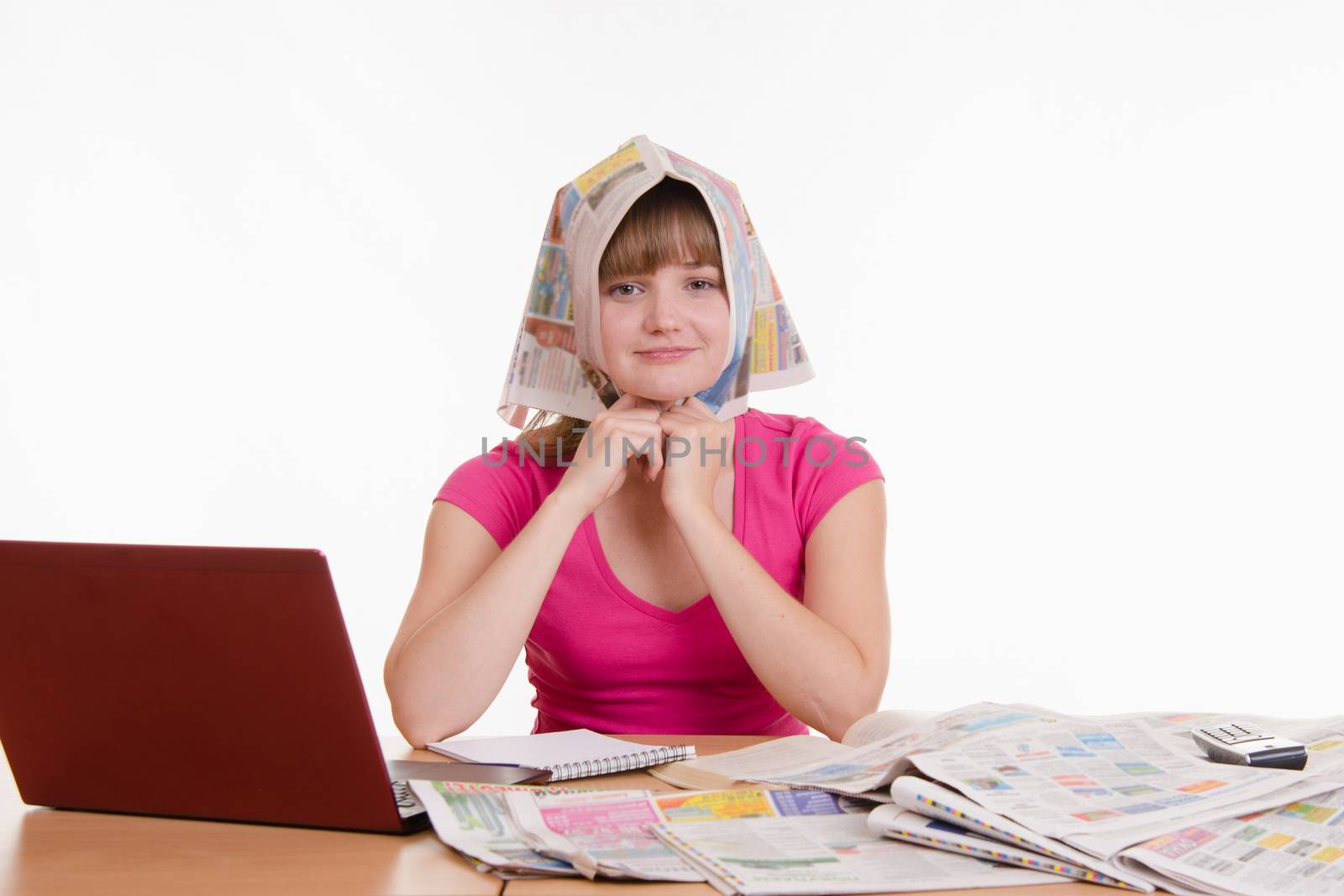A young girl sits at a table with a pile of newspapers, encyclopedias and a laptop