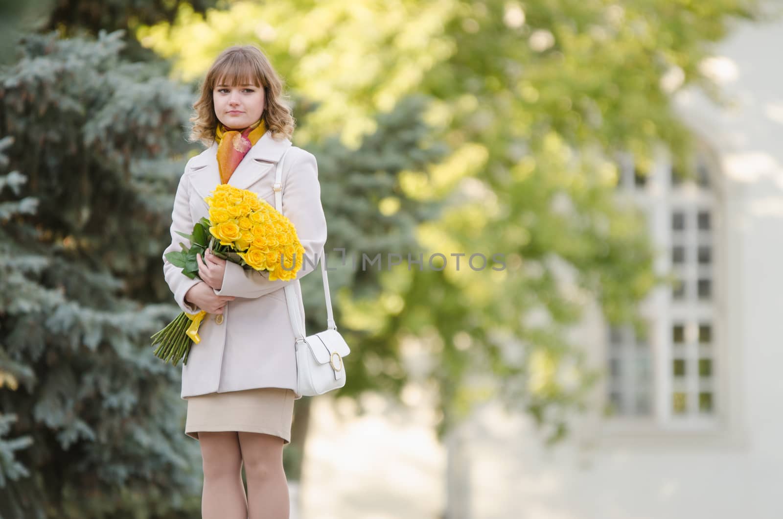 Young cute girl with a bouquet of yellow roses walks in autumn cool weather