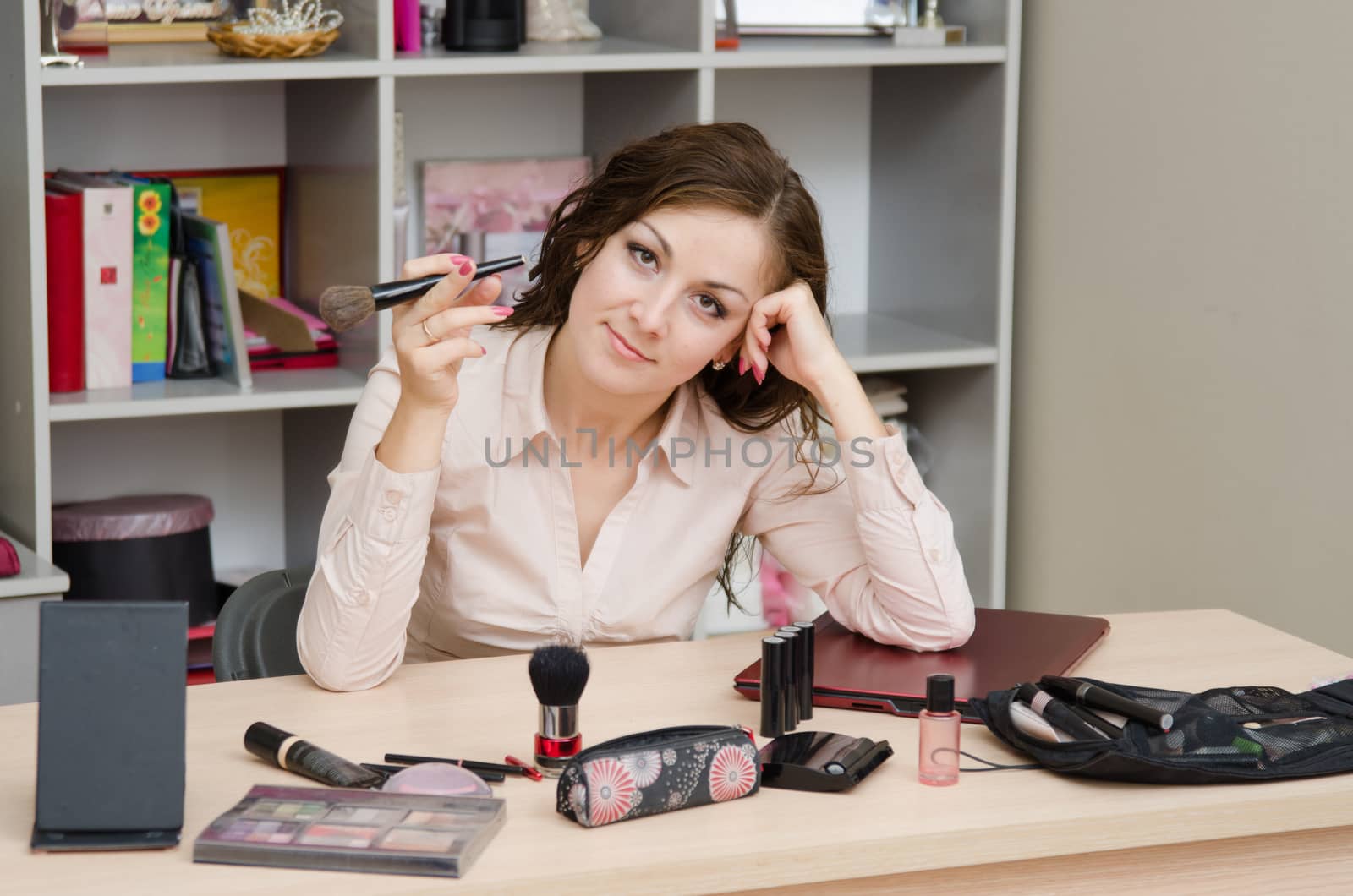 Young woman sitting at office table, laid out on the table cosmetics