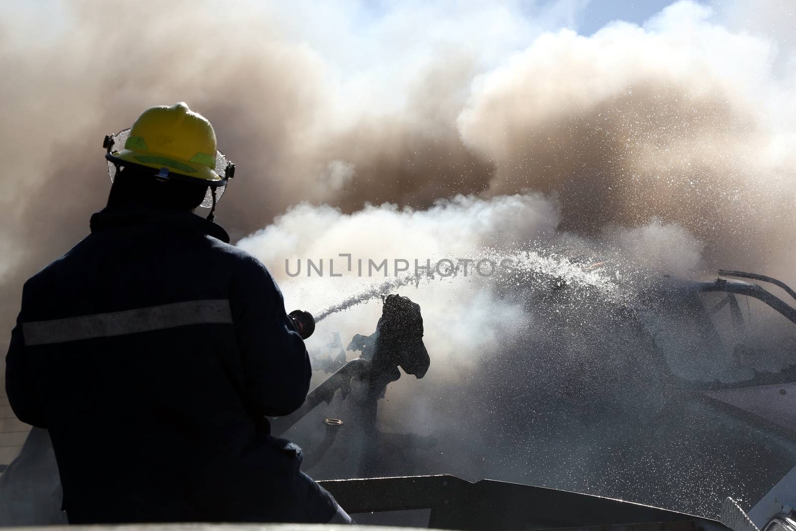 Fireman spraying water on a burnt out and smoking vehicle