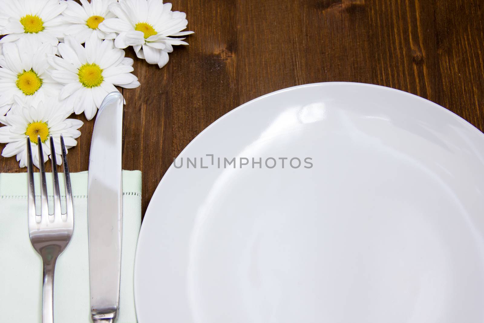 Cutlery and plate with flowers on wooden table seen up close