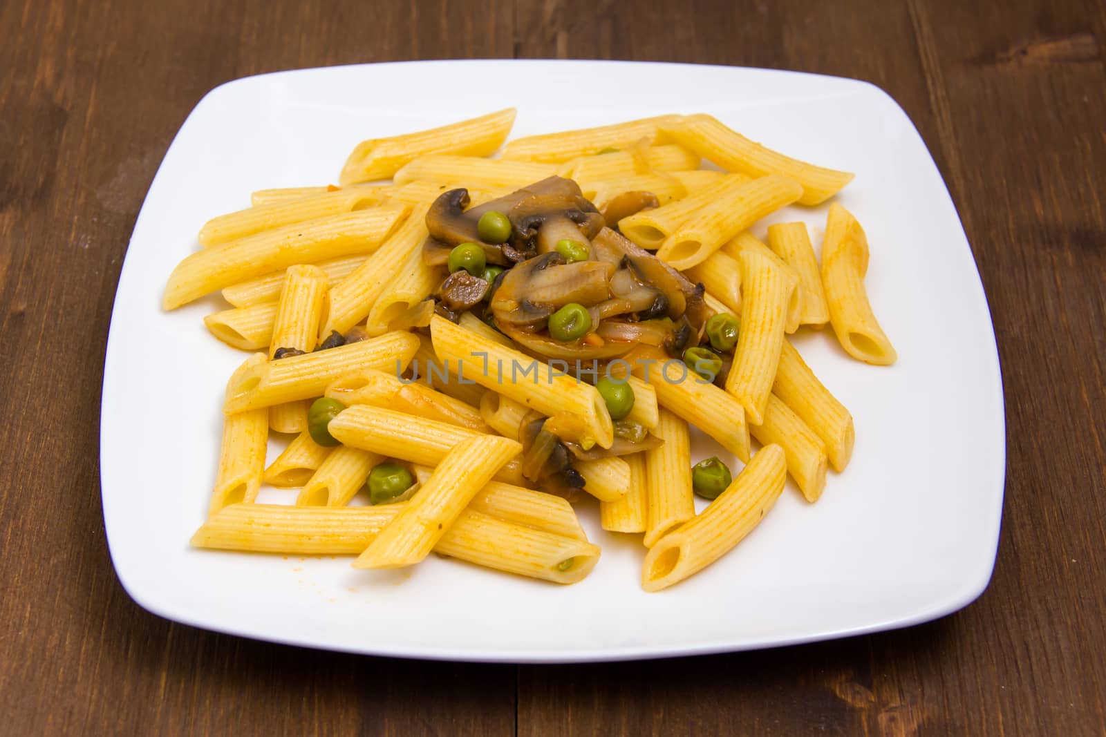 Pasta with mushrooms and peas on wooden table