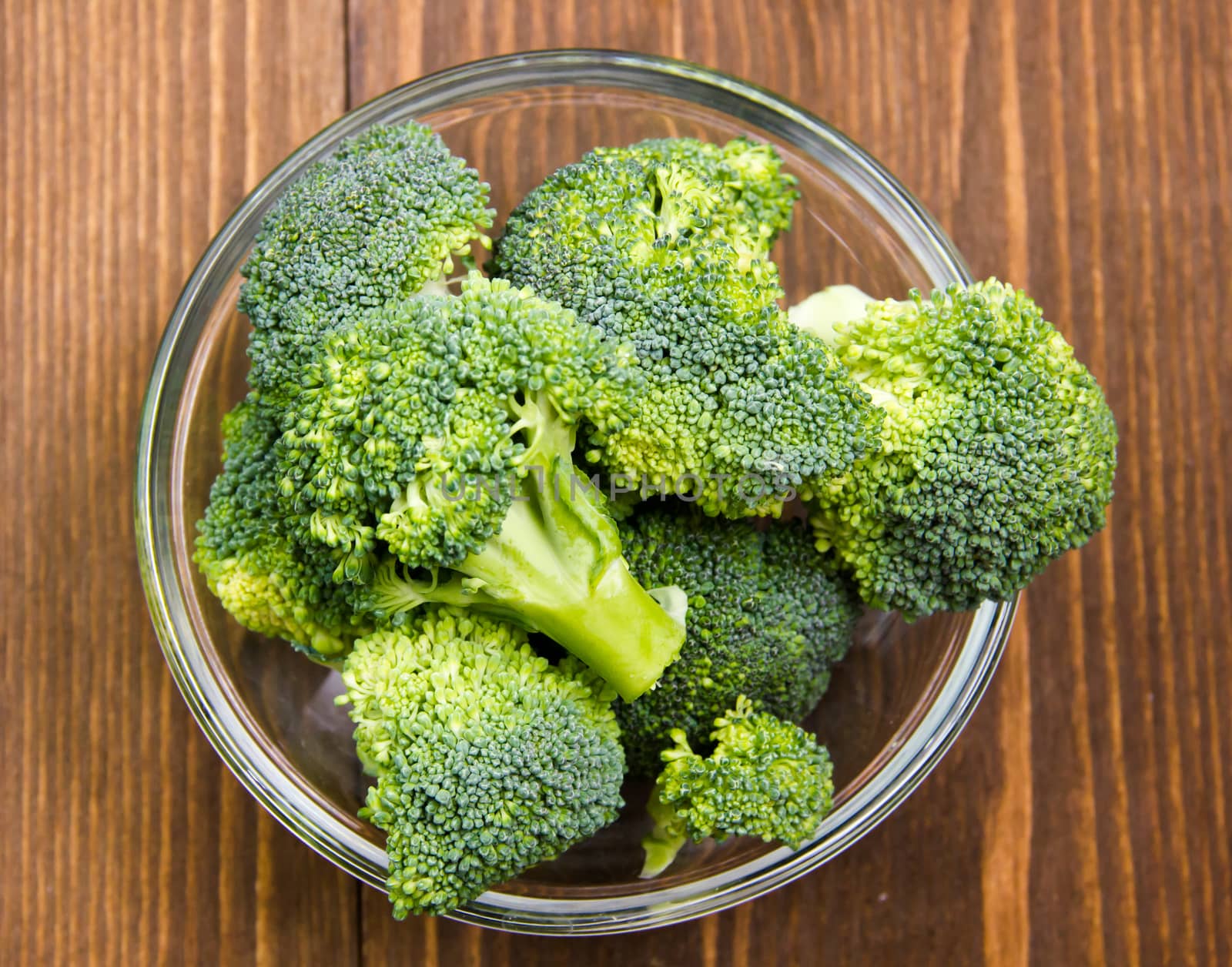 Broccoli in glass bowl on wooden table seen from above