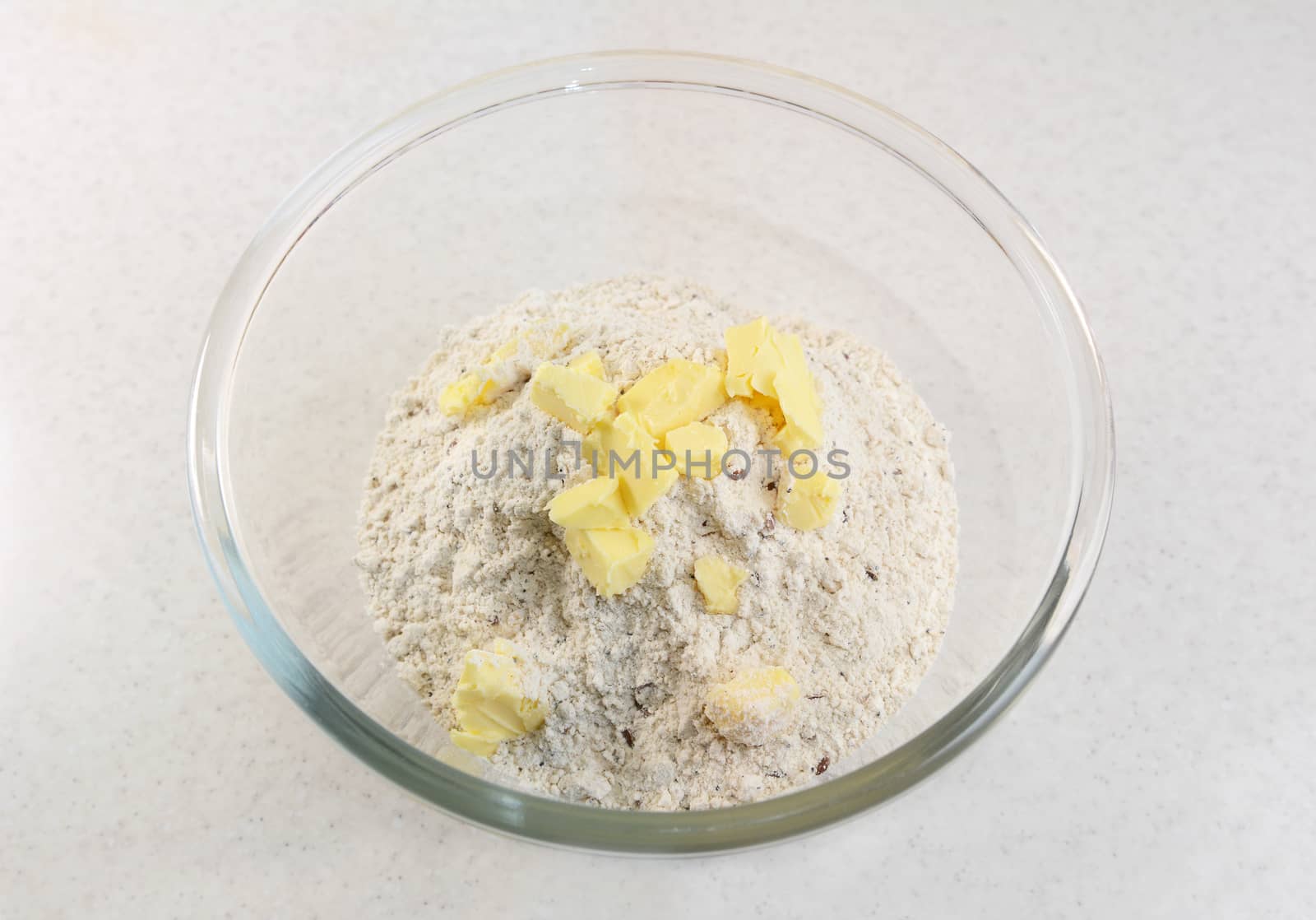 Adding pats of butter to a bread flour mix in a glass bowl