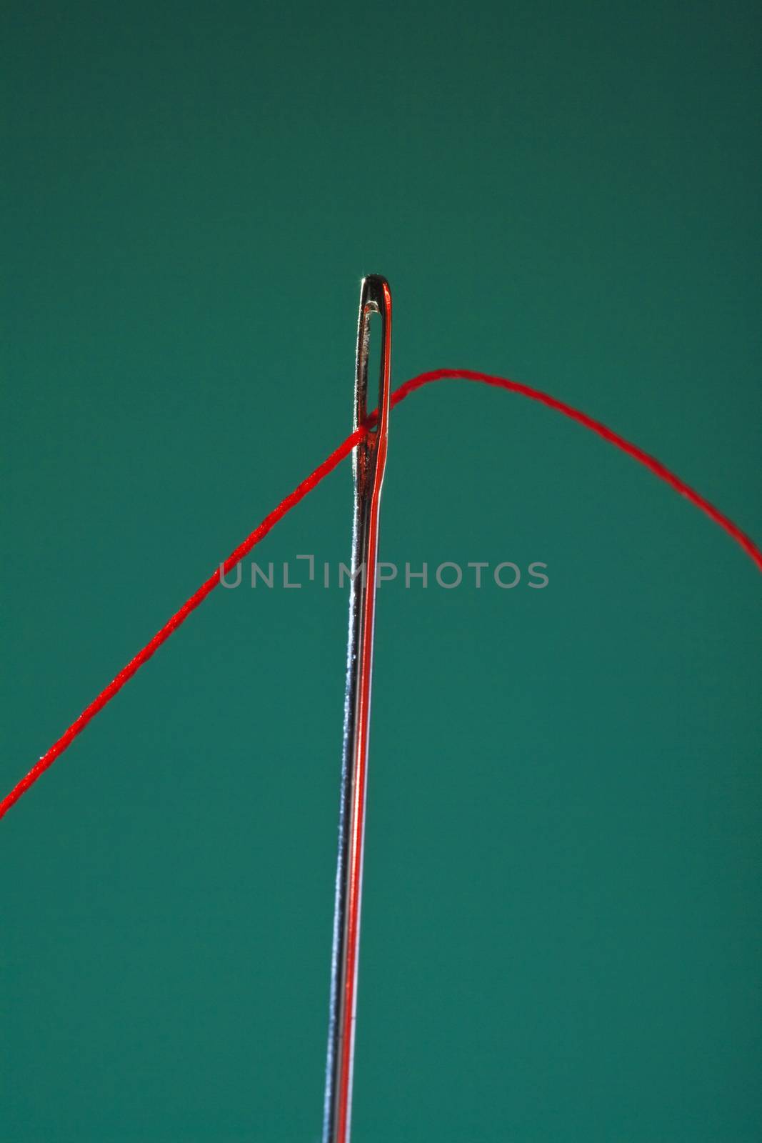 macro image of needle and red thread against colorful background