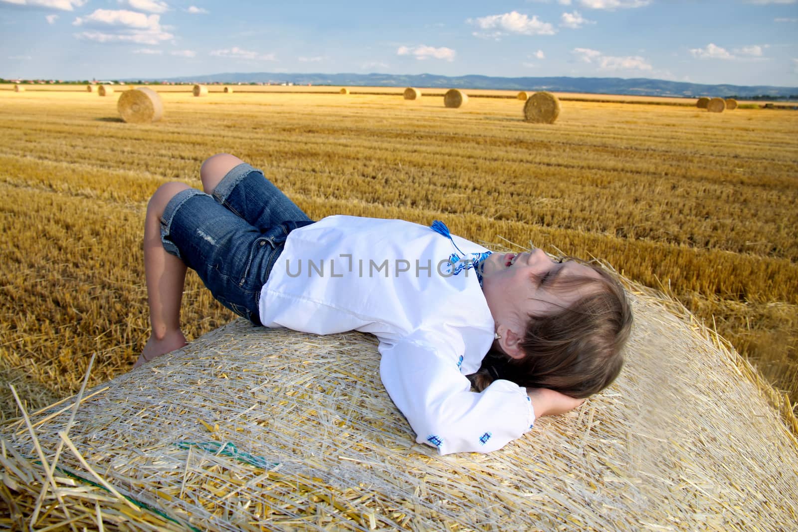 small rural girl on the straw after harvest field with straw bales
