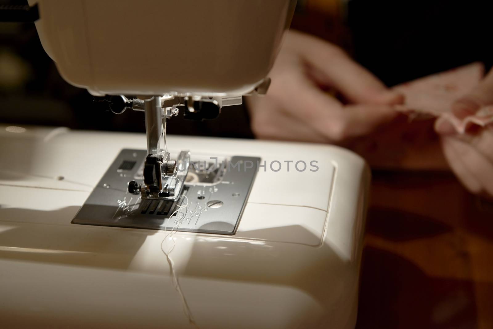Detail of automatic sewing machine with hands working on piece of fabric in the background
