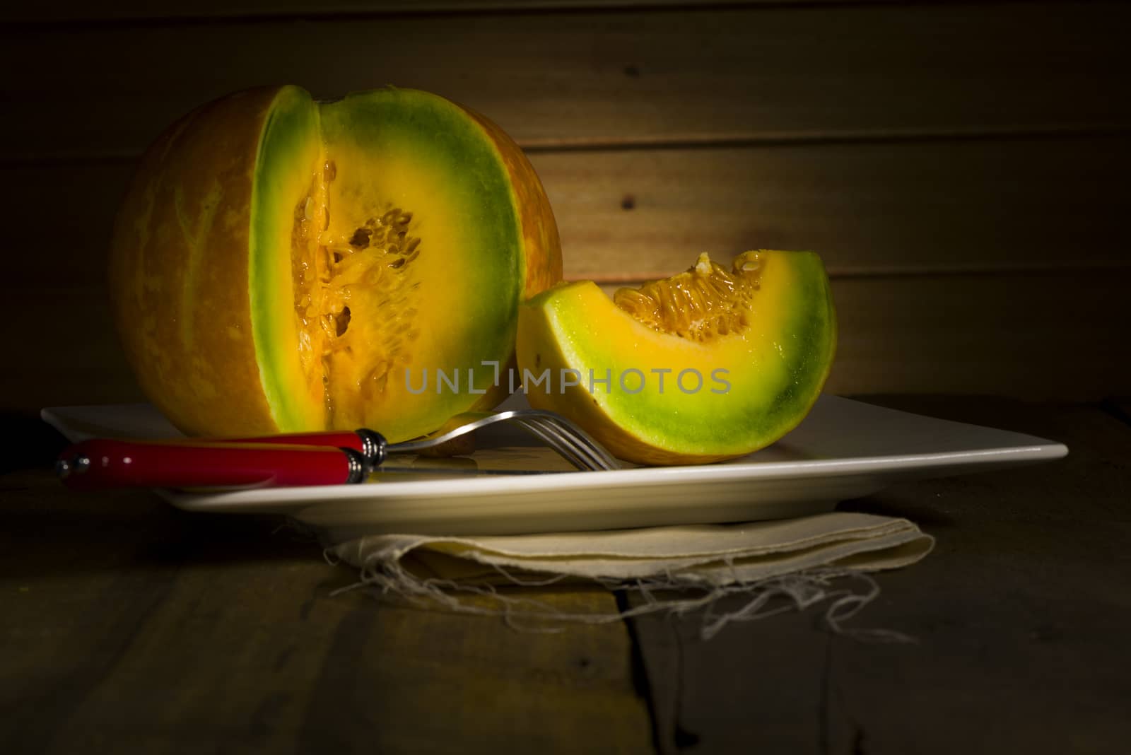 Sliced ripe spanspek, cantaloupe or sweet melon served on a platter on a table in front of a wooden wall with utensils for a healthy dessert