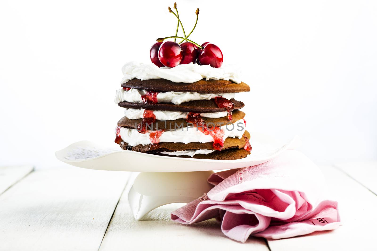 Chocolate cake with cherries and vanilla cream on an white wood table