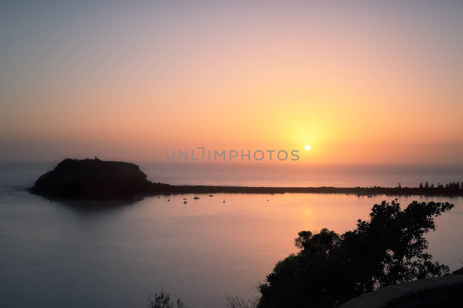 New Years Day sunrise overlooking Broken Bay,  Pittwater, Palm beach  adn Barenjoey Lighthouse and headland. A mist or fog diffusing the light and reducing visibility, cargo ship  and horizon line barely noticeable