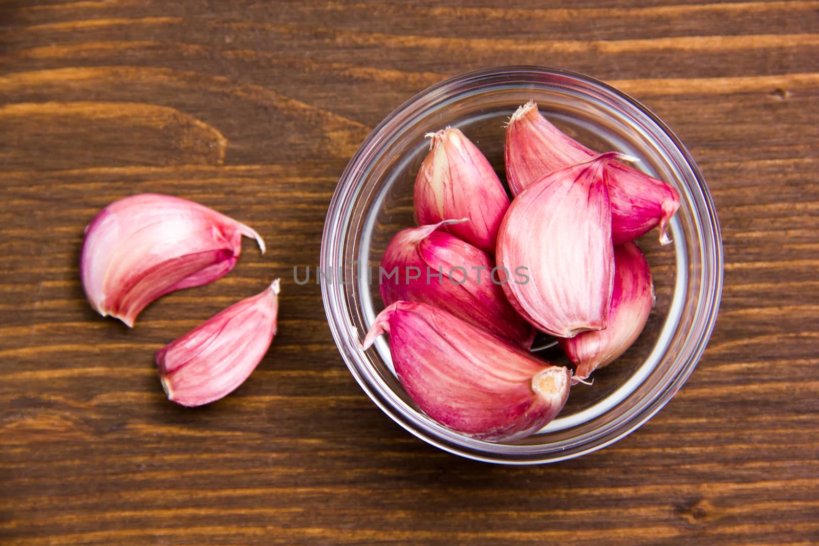 Garlic in glass bowl on wooden table seen from above