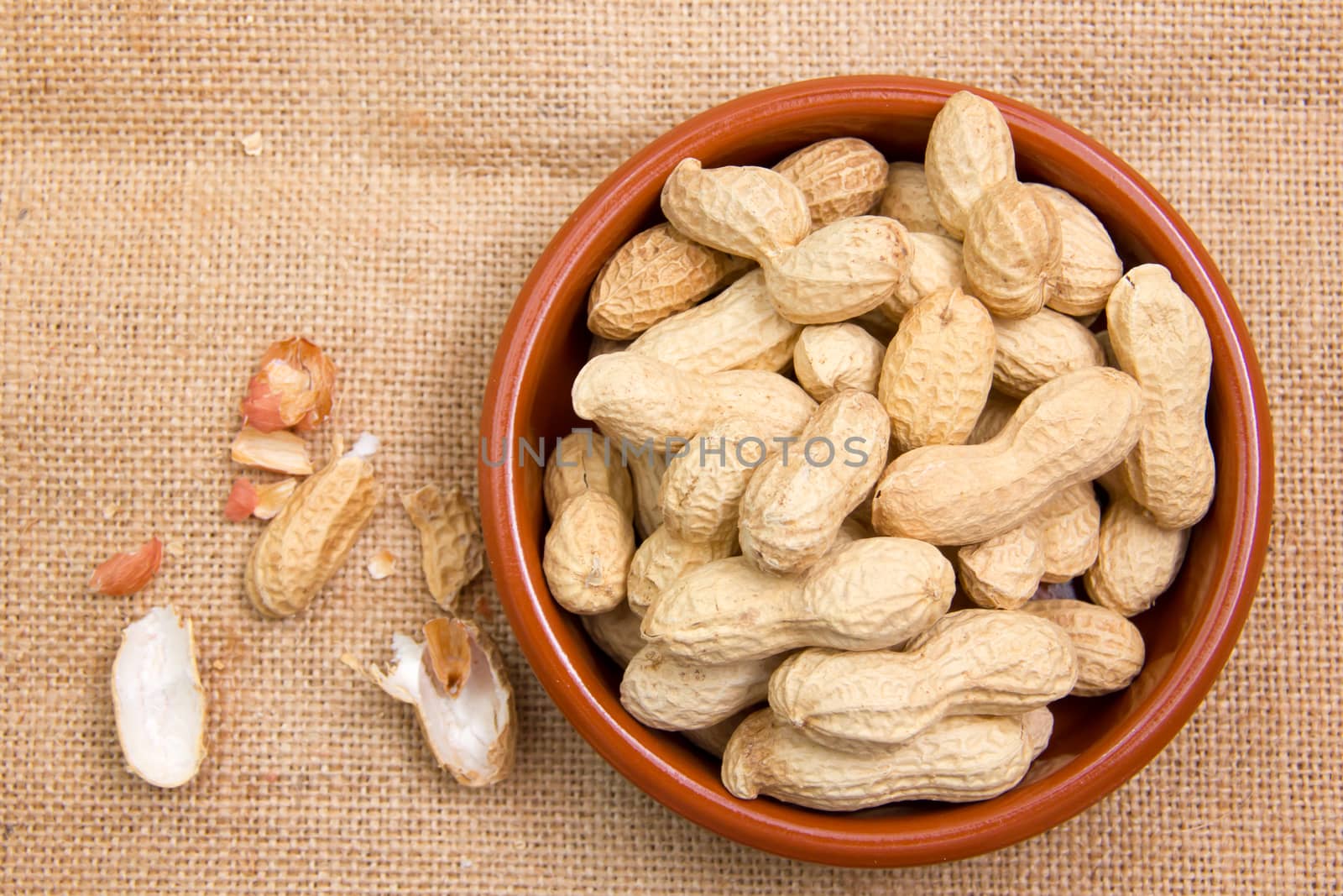 Peanuts in rustic bowl on jute mat seen from above