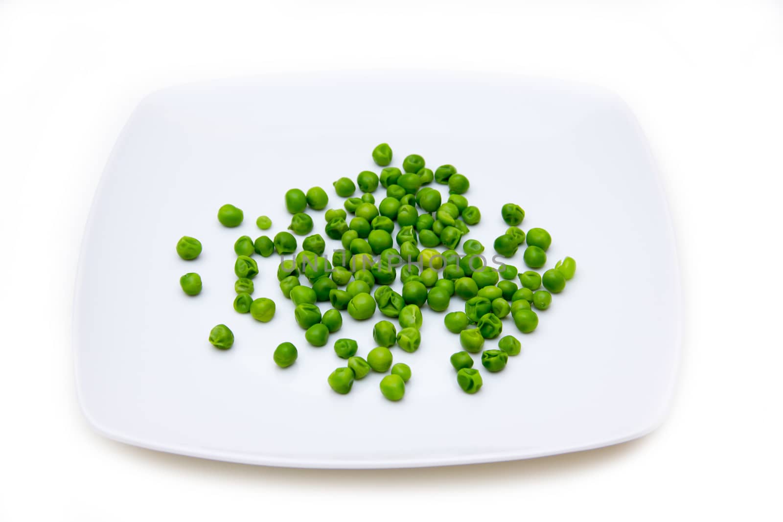 Plate with cooked green peas on a white background