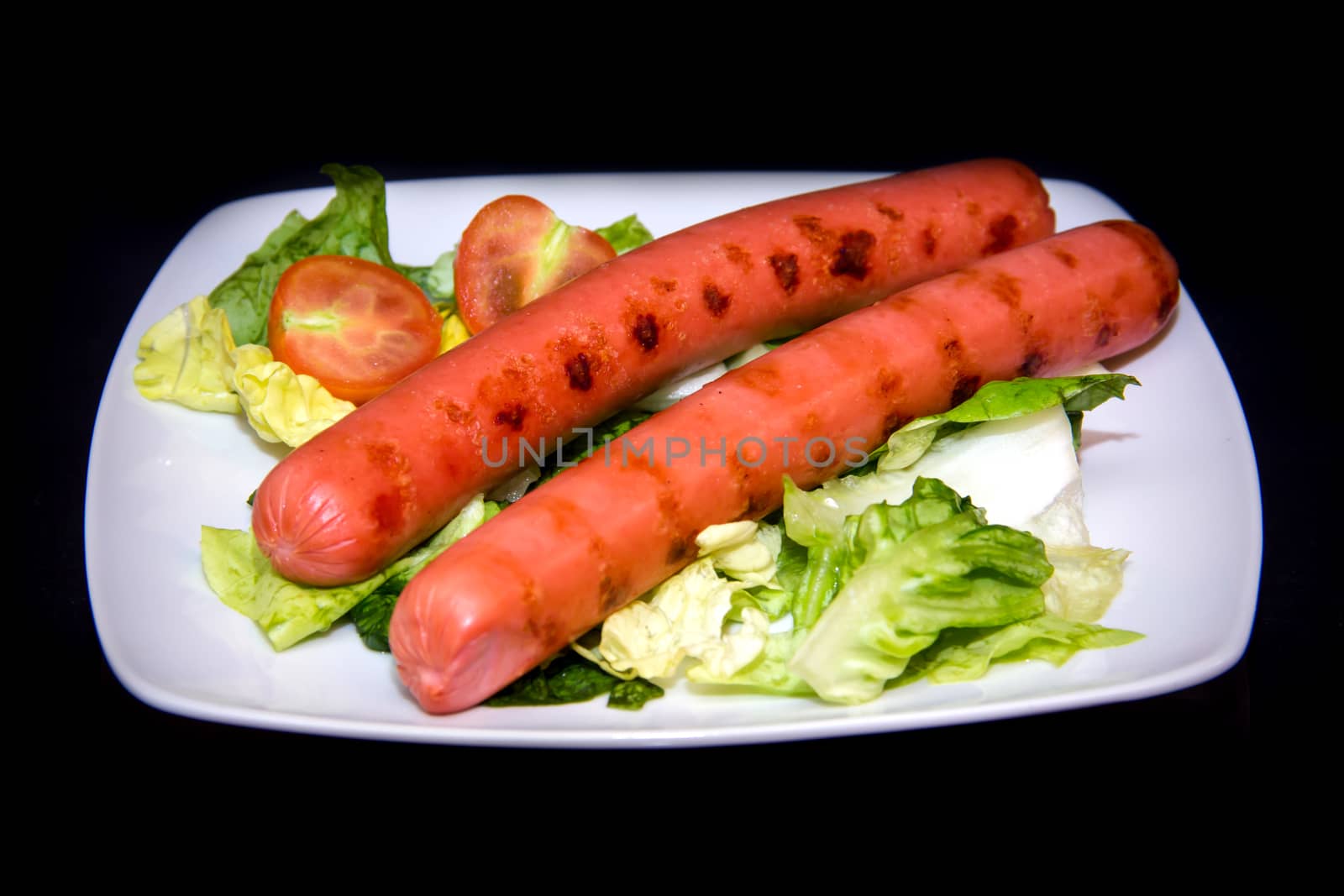 Sausages with salad on plate on black background