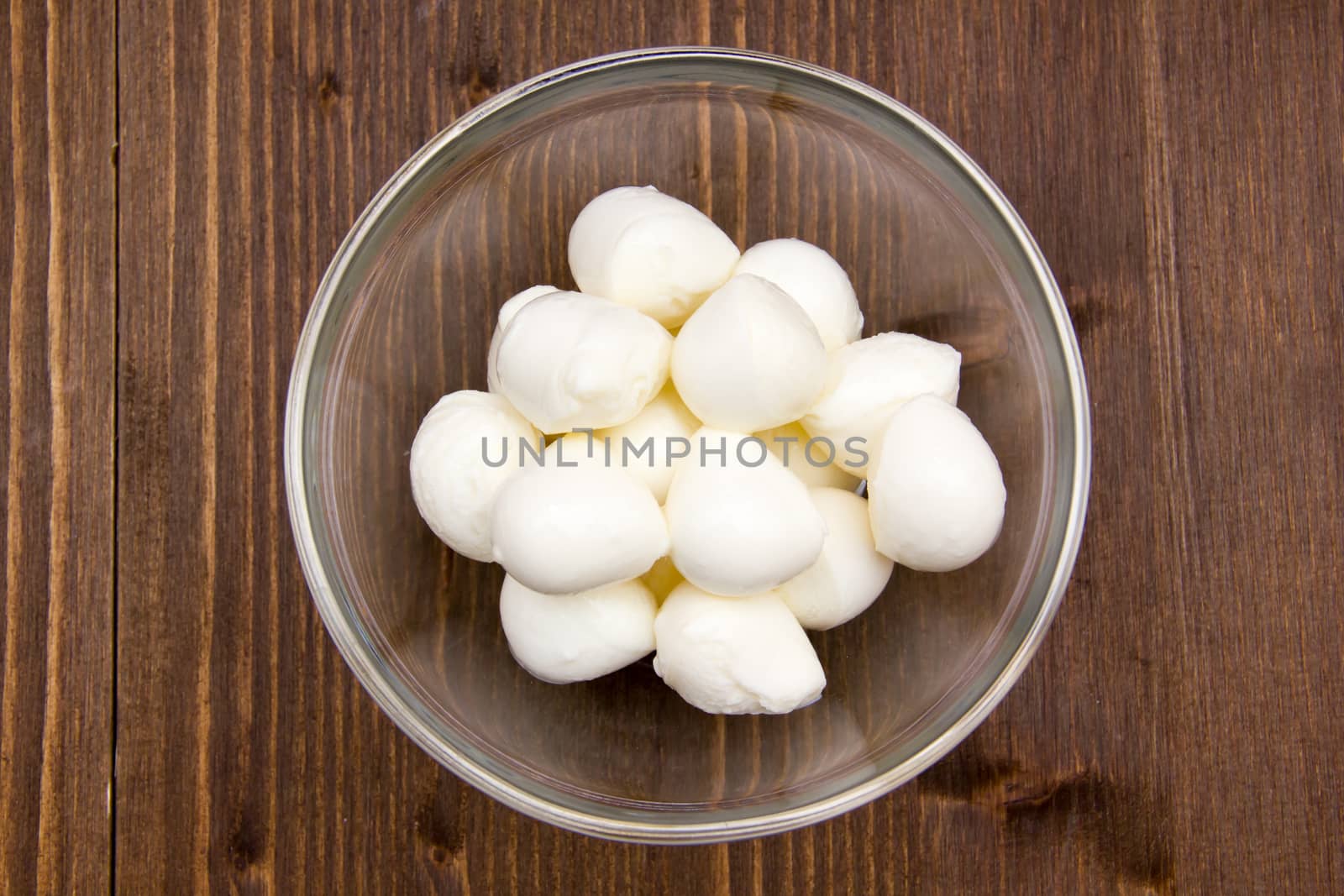 Small mozzarella in bowl on wooden table seen from above