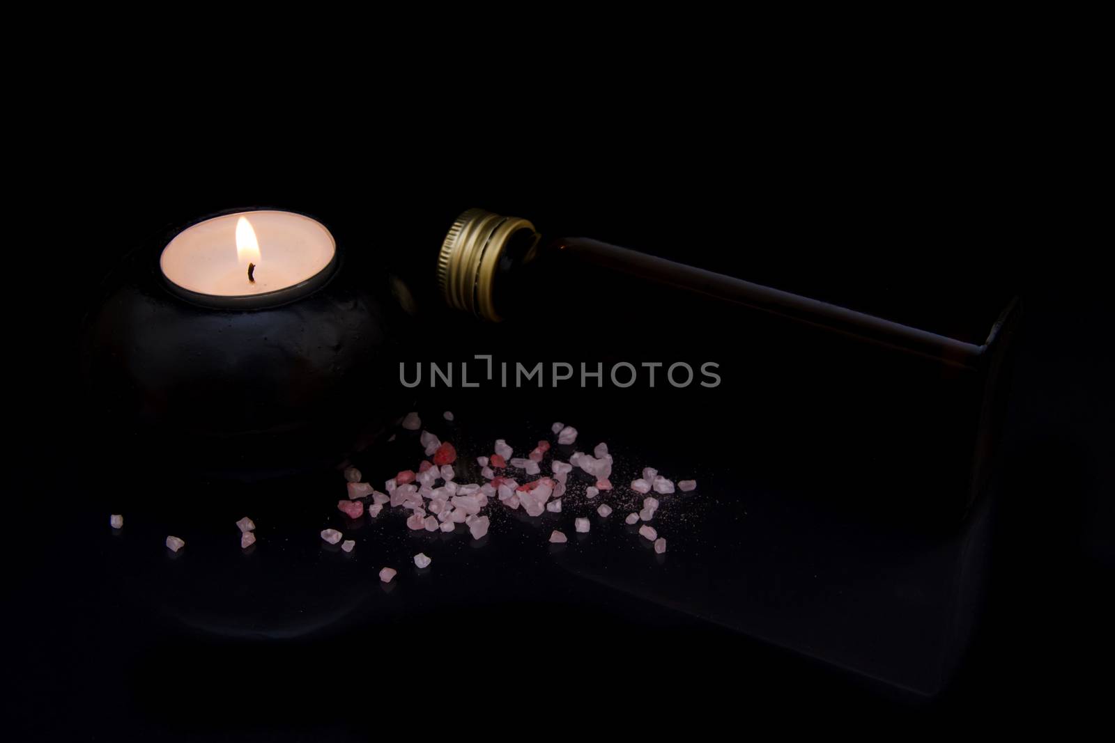 Candle with bath salts and oil on black background