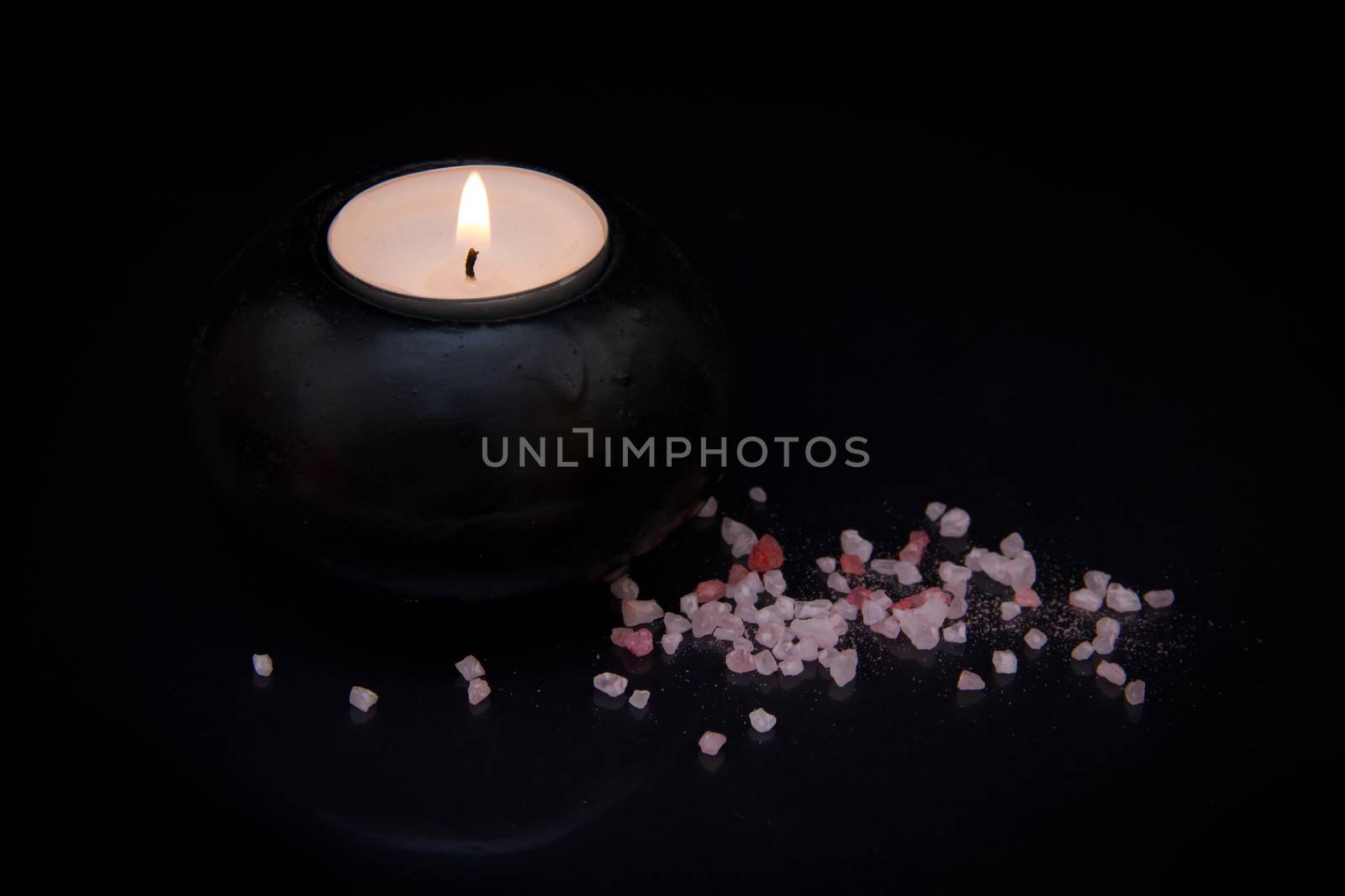 Candle with bath salts on black background