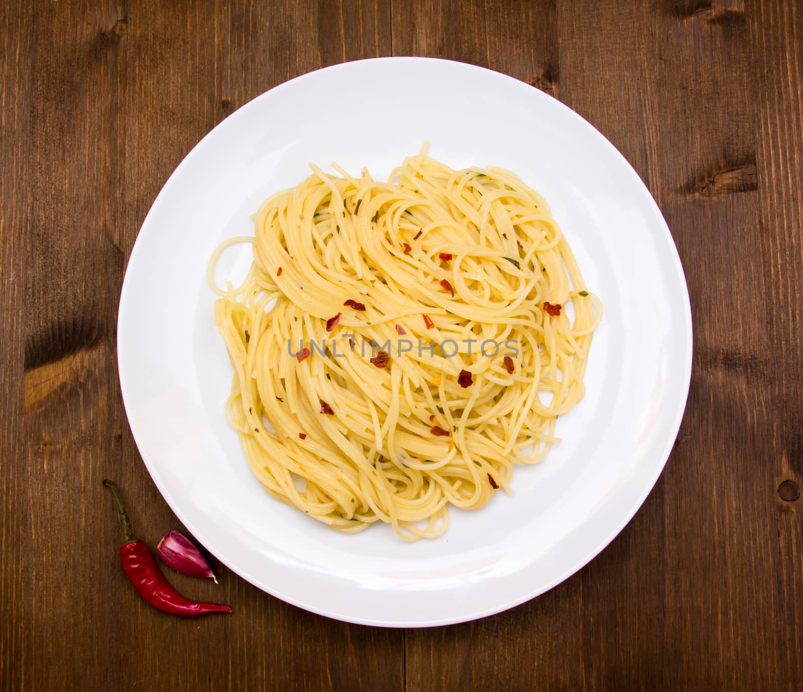 Spaghetti with garlic and chili peppers on wooden table seen from above