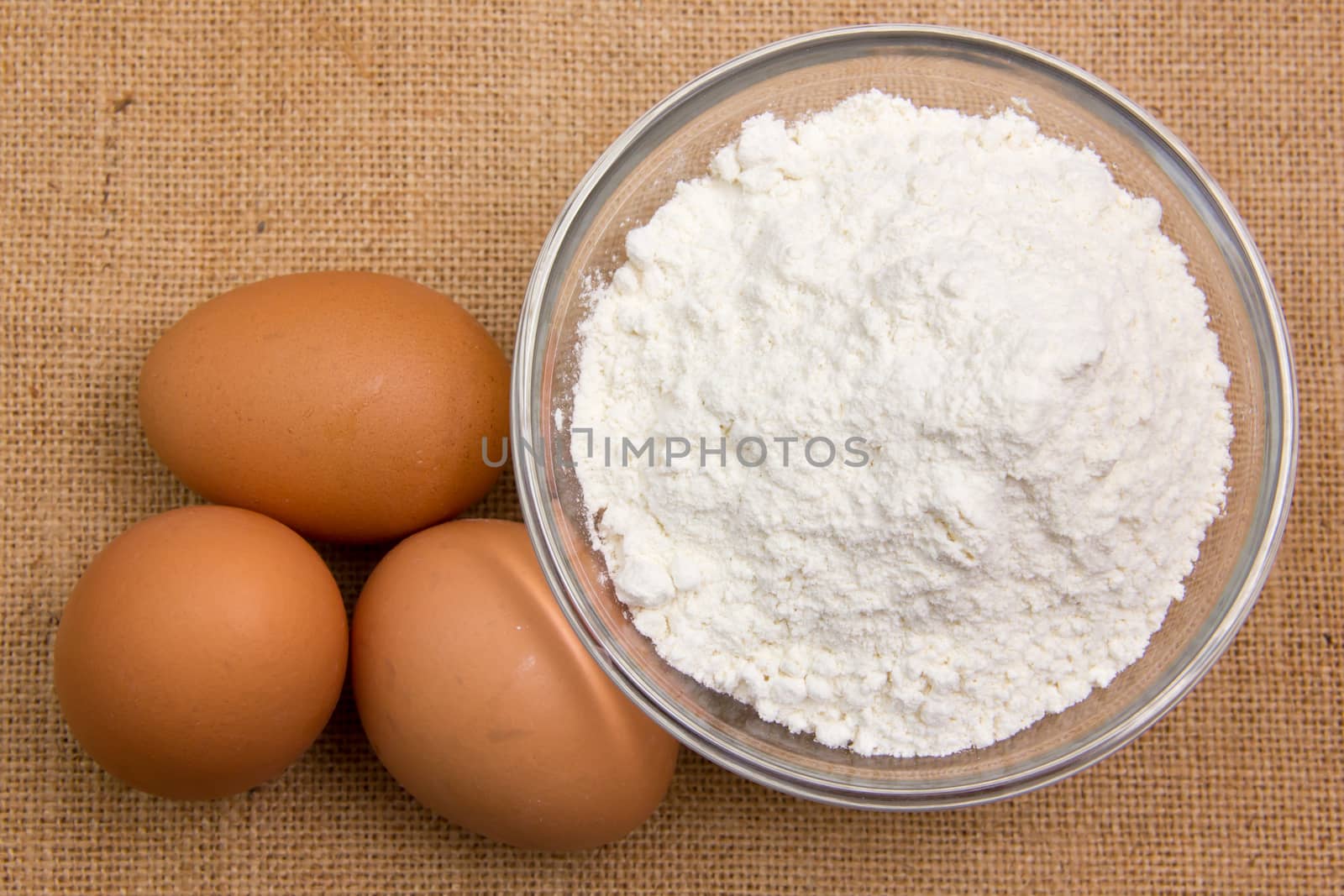 Eggs and flour in bowl on jute tablecloth viewed from above